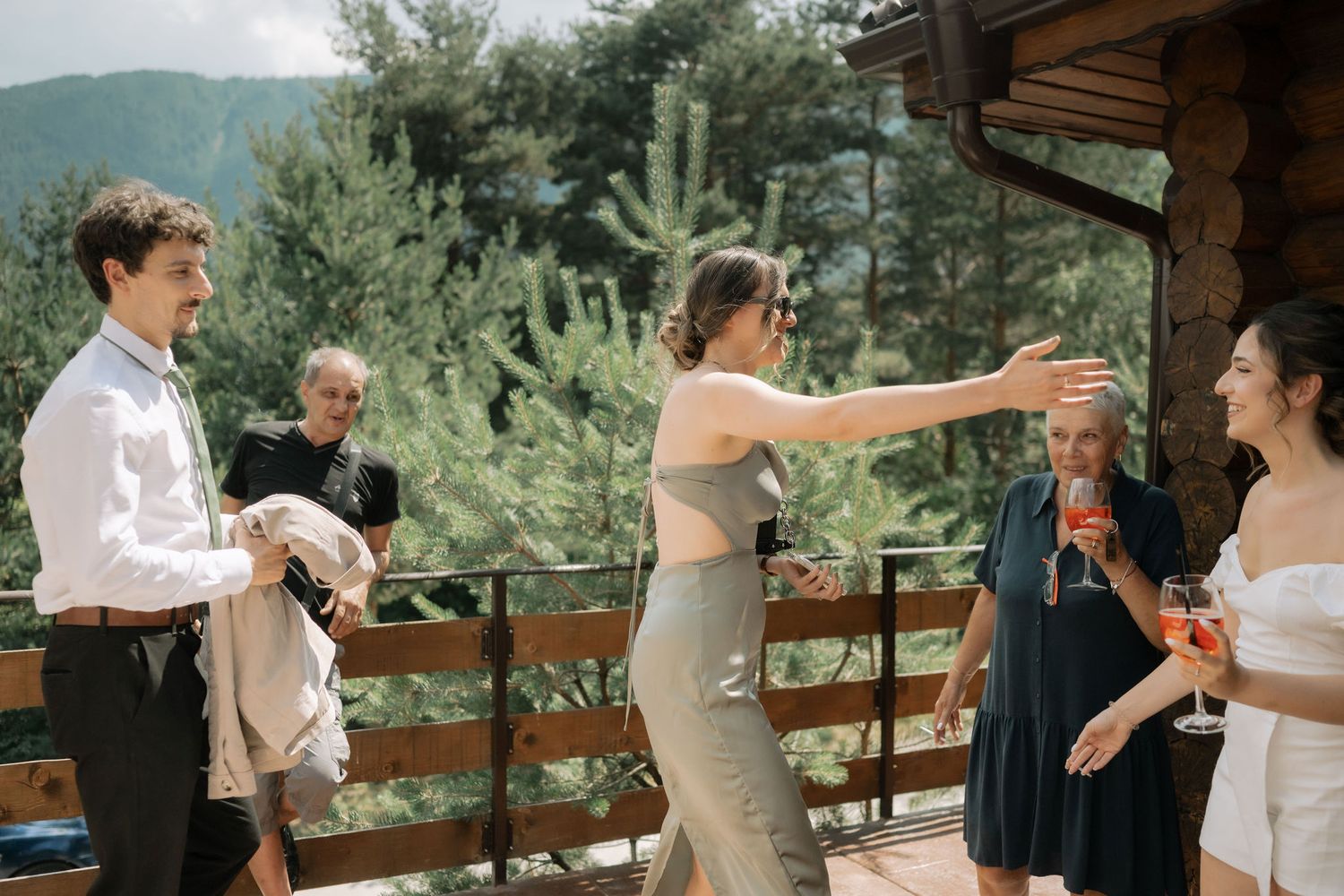 Wedding guests share a joyful moment on a rustic wooden deck overlooking mountain scenery.