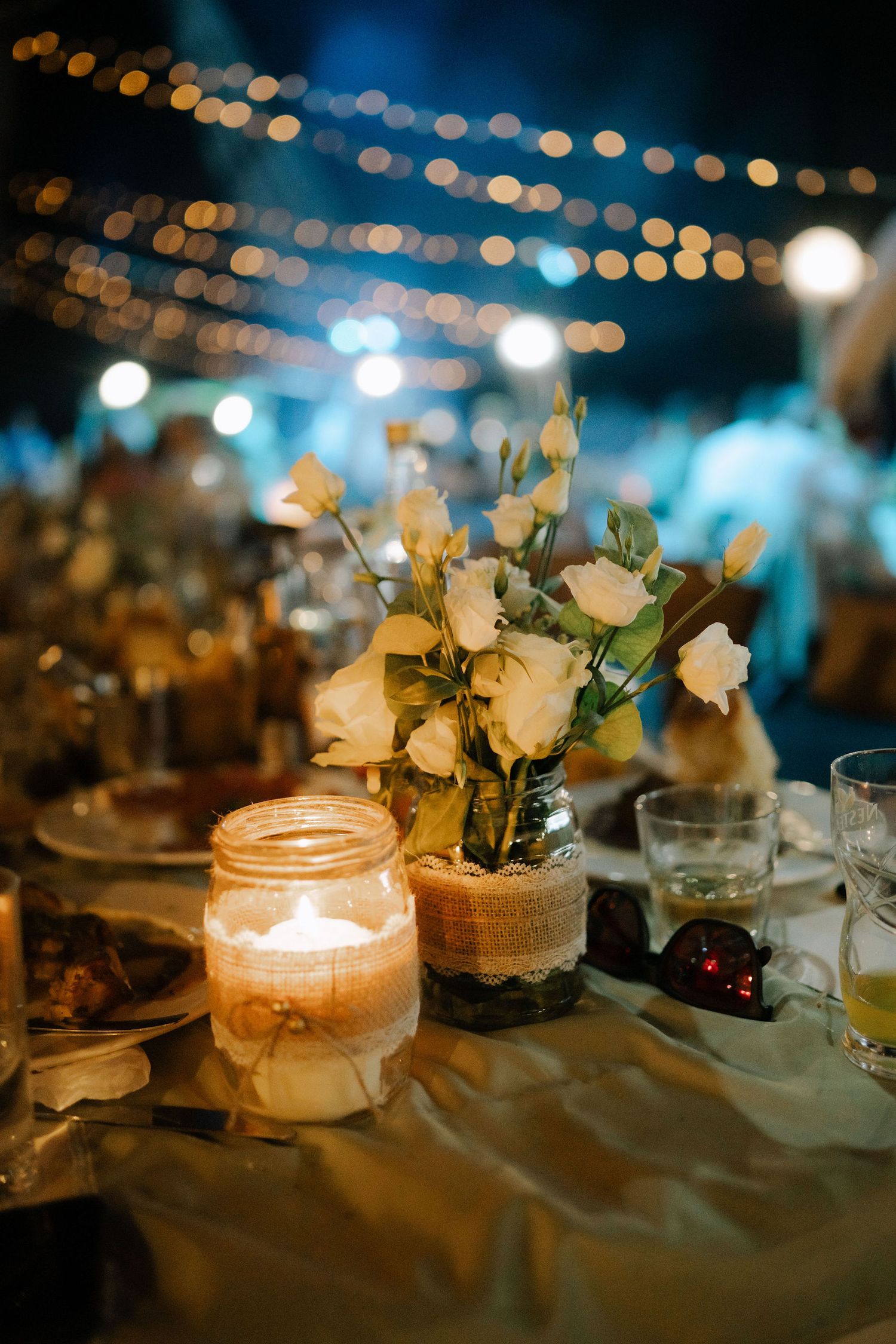 Romantic candlelit mason jar centerpieces with white flowers create an elegant evening ambiance at a wedding reception.
