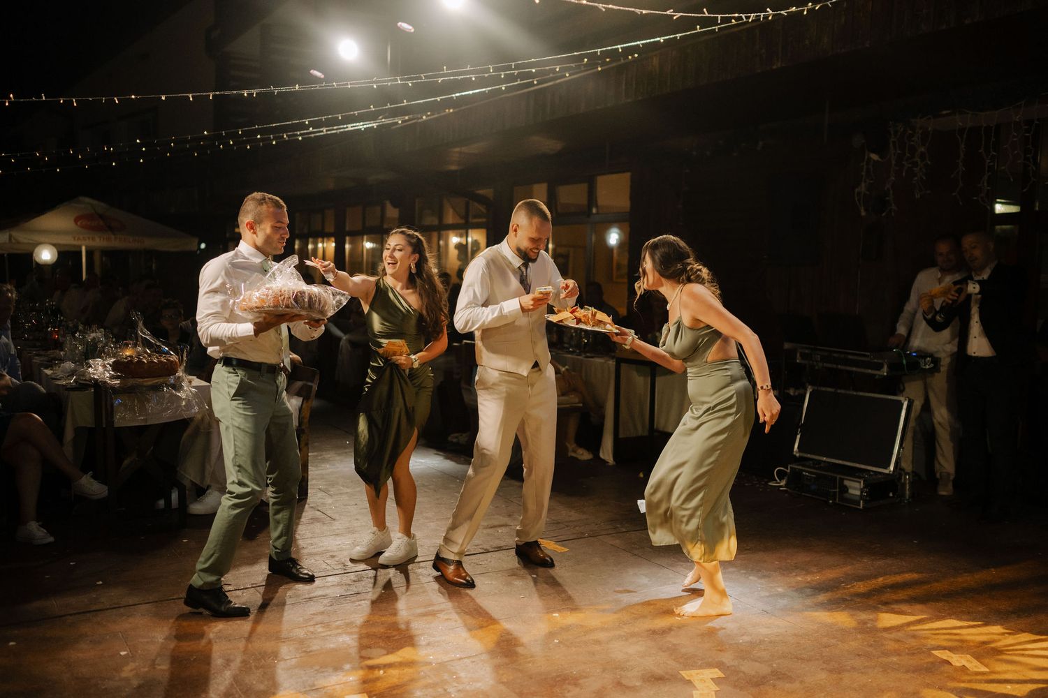 People dance together on a wooden floor under warm lighting at an evening celebration event.
