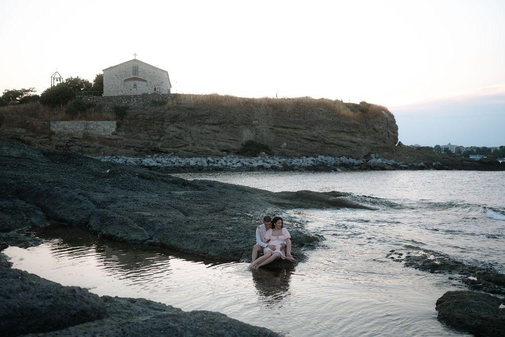 A small boat navigates through rocky coastal waters near a white building perched on a cliff at dusk.