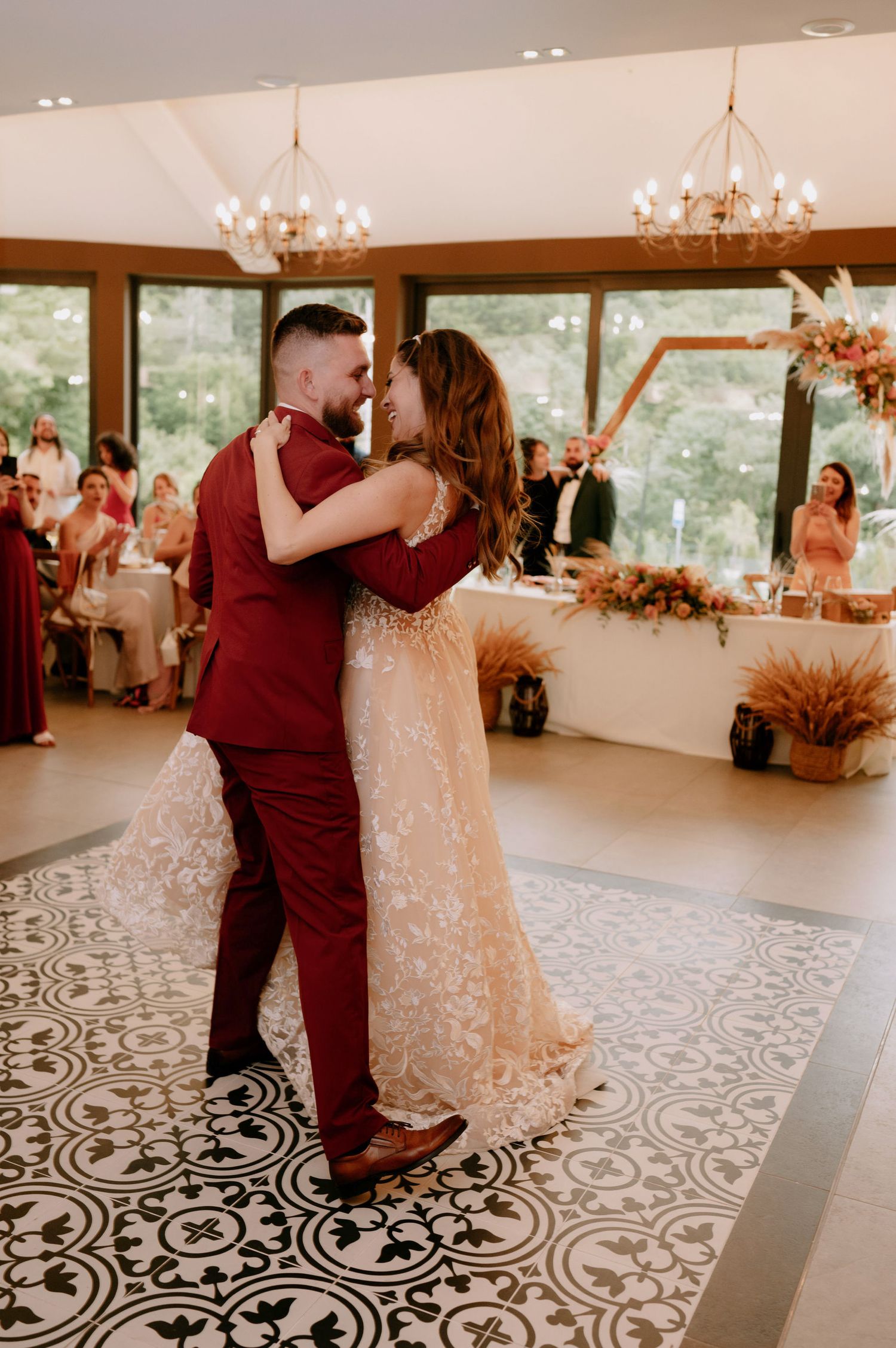 A couple shares their first dance at a wedding reception on a black and white patterned floor under chandeliers.
