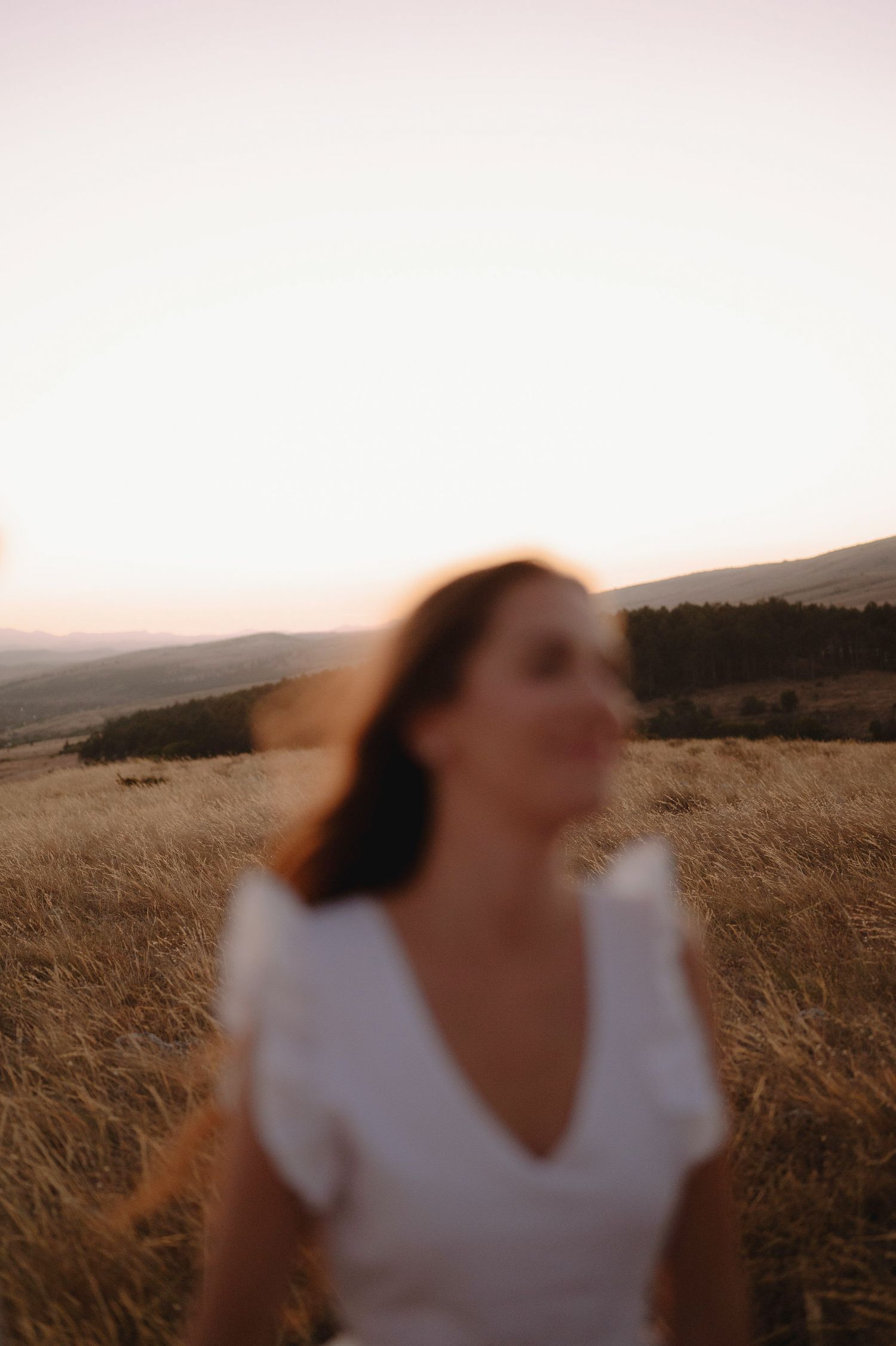 A woman in a white dress spins joyfully in a golden wheat field at sunset.