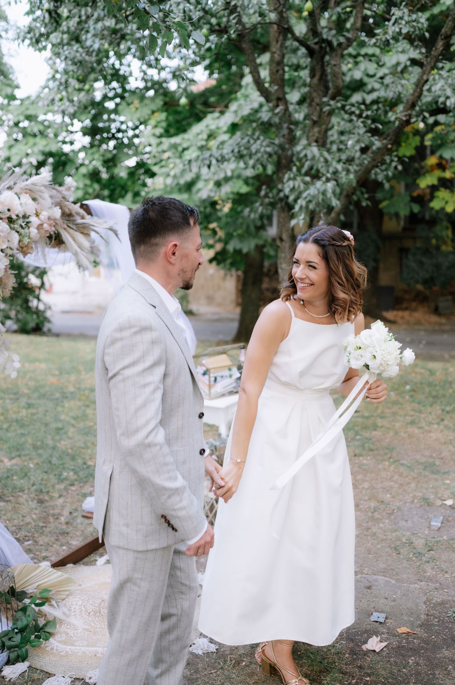 A couple shares a joyful moment at their outdoor wedding ceremony, with the bride holding a white bouquet.