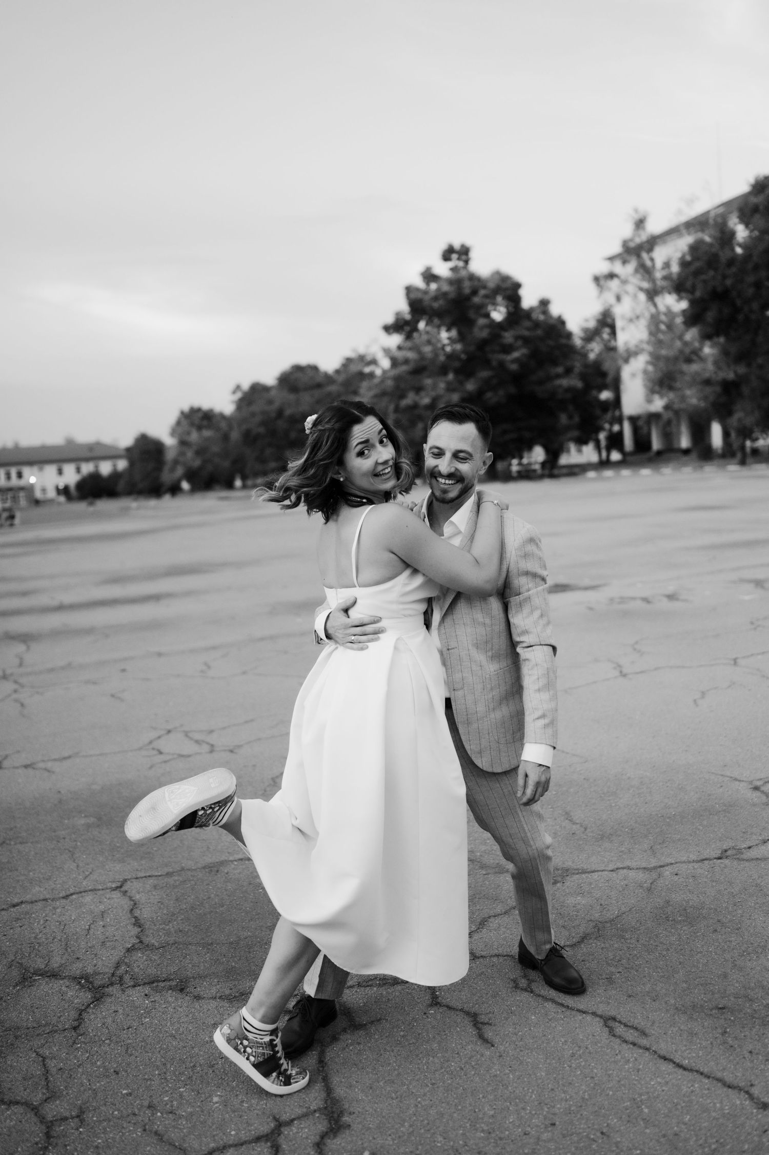 A couple dances playfully outdoors in black and white, with the bride wearing a white dress and sneakers.
