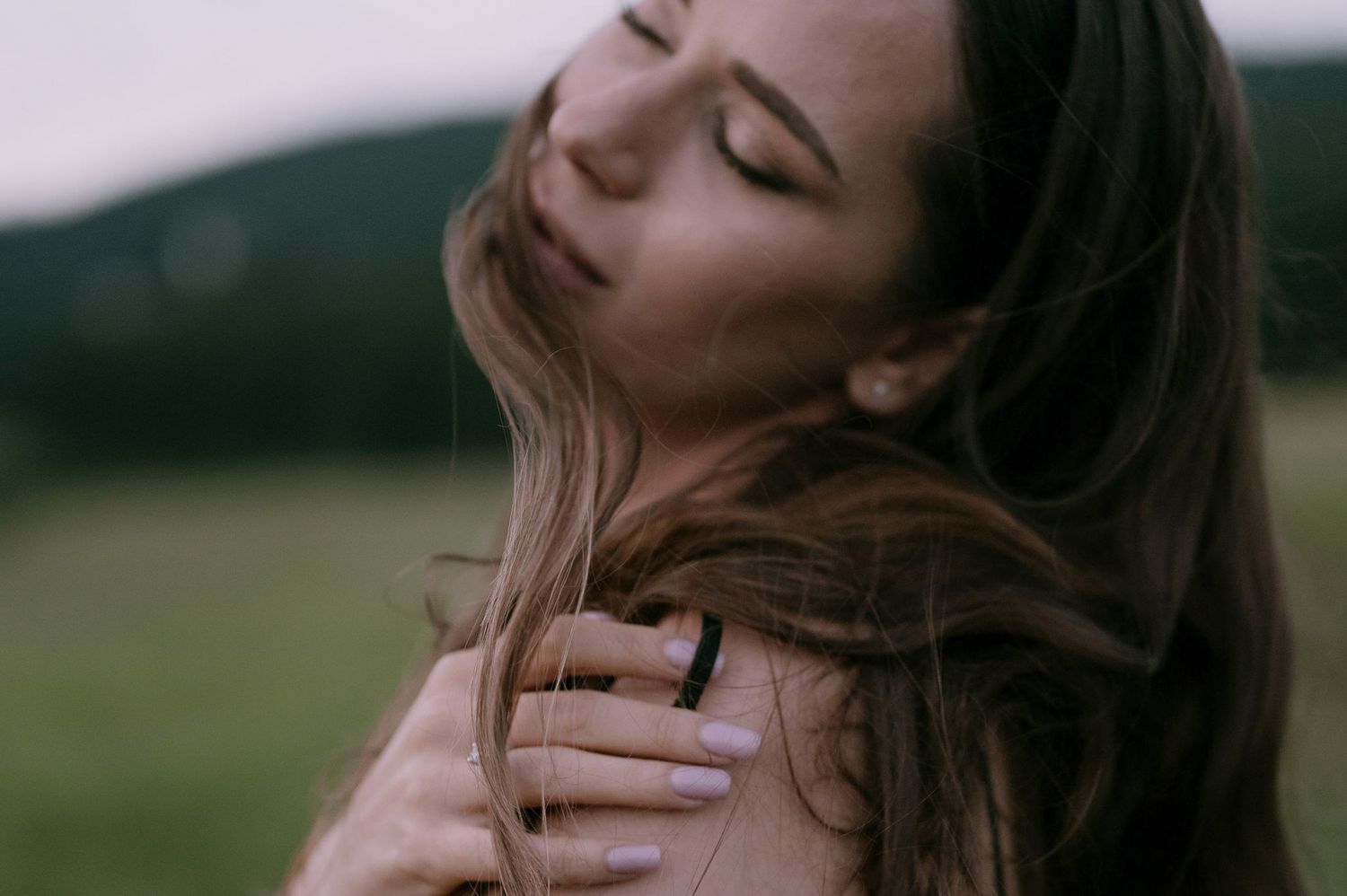 A woman with flowing brown hair is shown in a series of candid expressions against a blurred outdoor background.