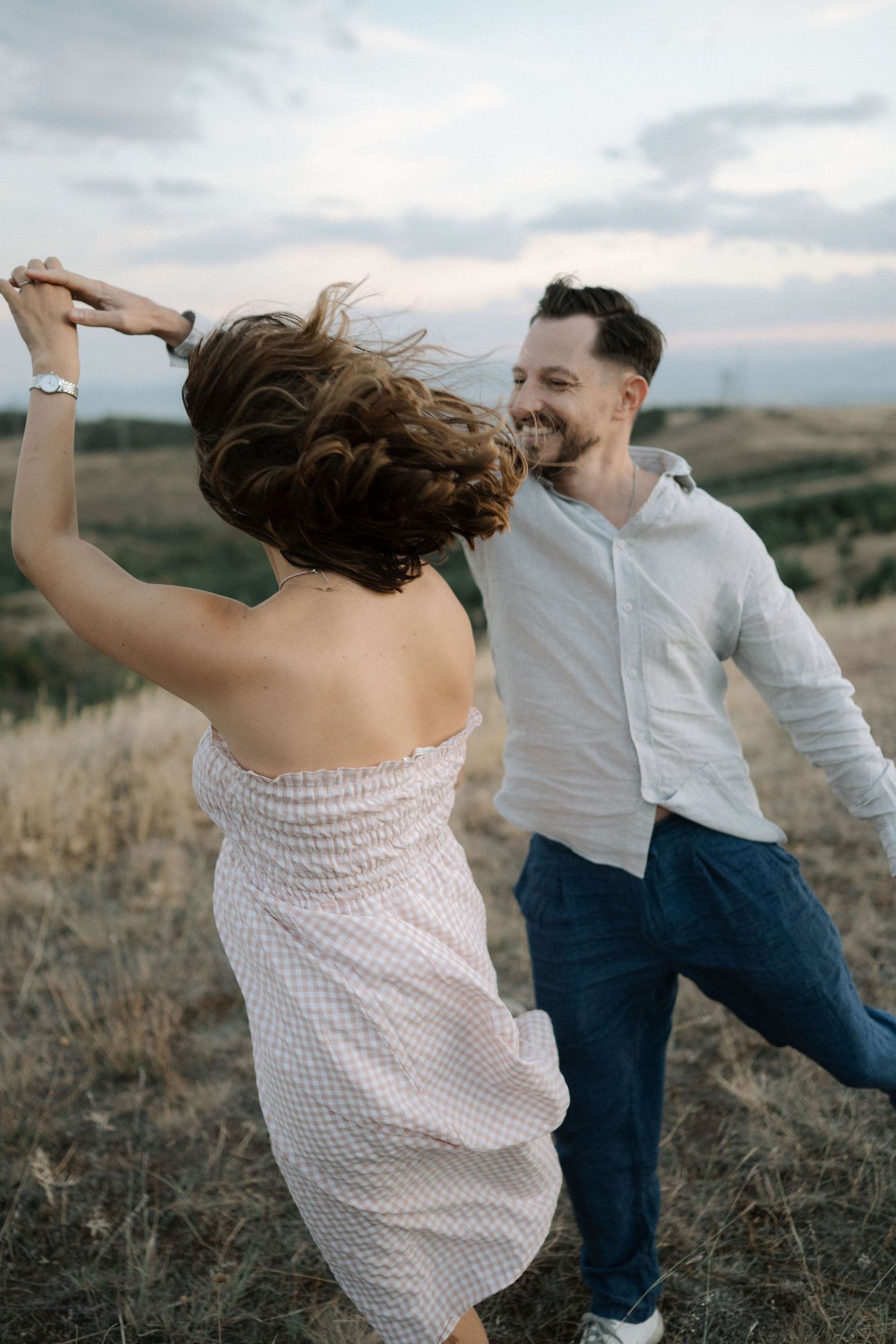 Couple dances playfully in a field at sunset, with flowing movement and joyful energy.