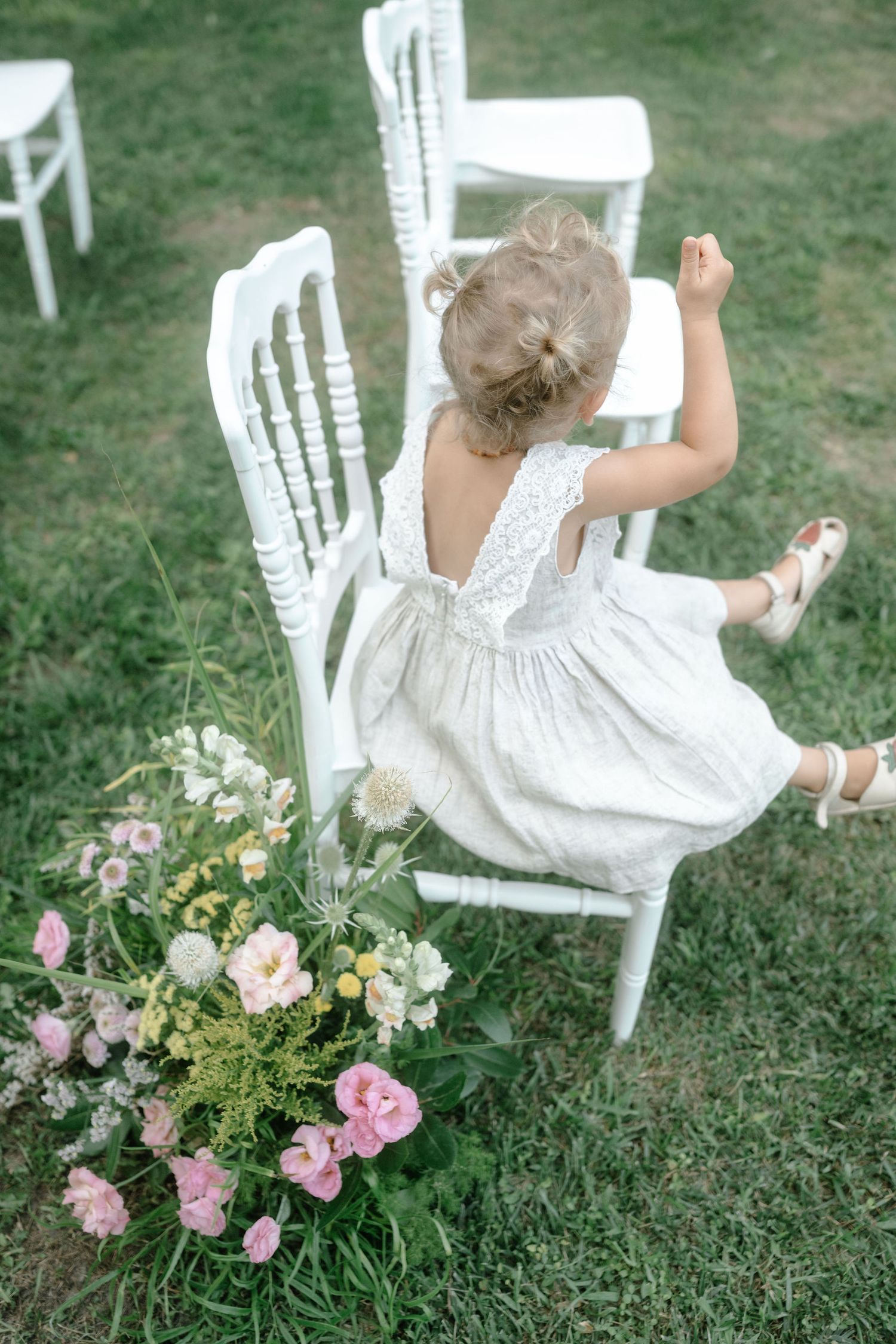 A white dress and floral arrangement on grass create a whimsical garden scene with delicate pink and white blooms.