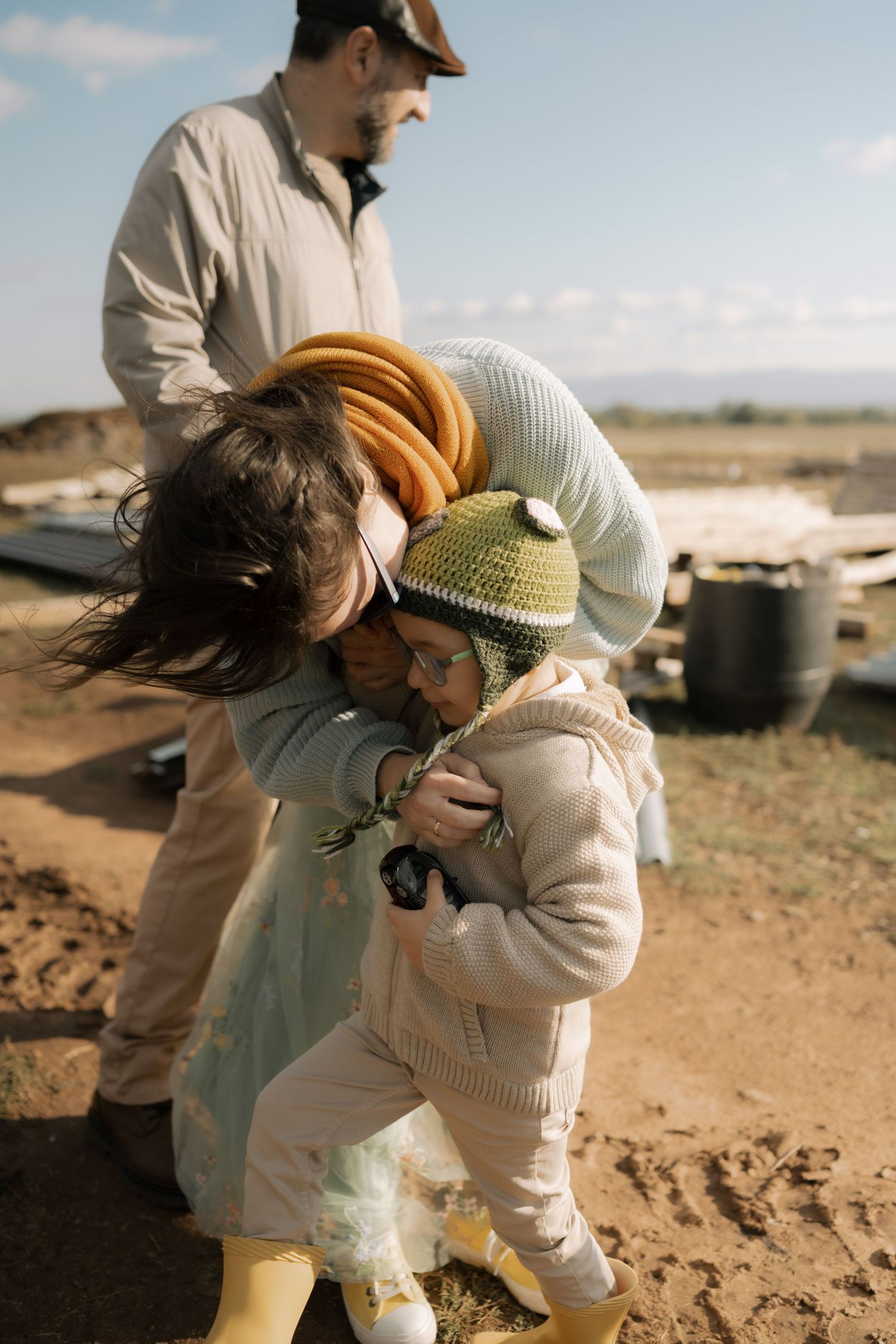 Two people in light colored clothing examine something while crouched on sandy terrain.