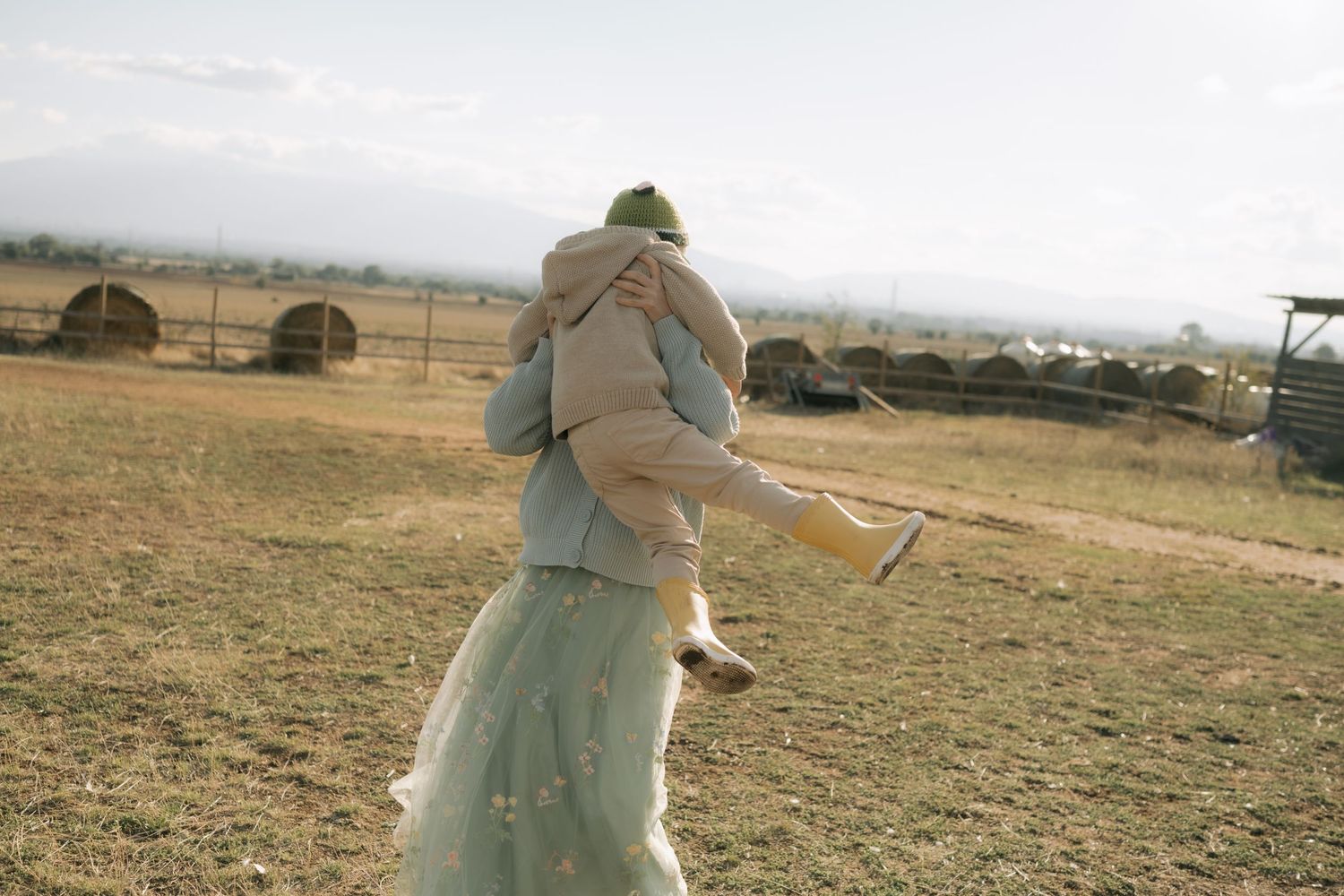 A person in a white protective suit walks across a dry field with metal structures visible in the background.