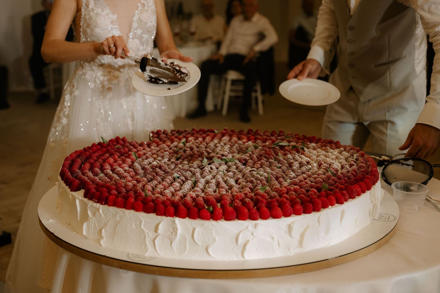 Bride and groom cutting a large round wedding cake topped with fresh strawberries and chocolate decorations.