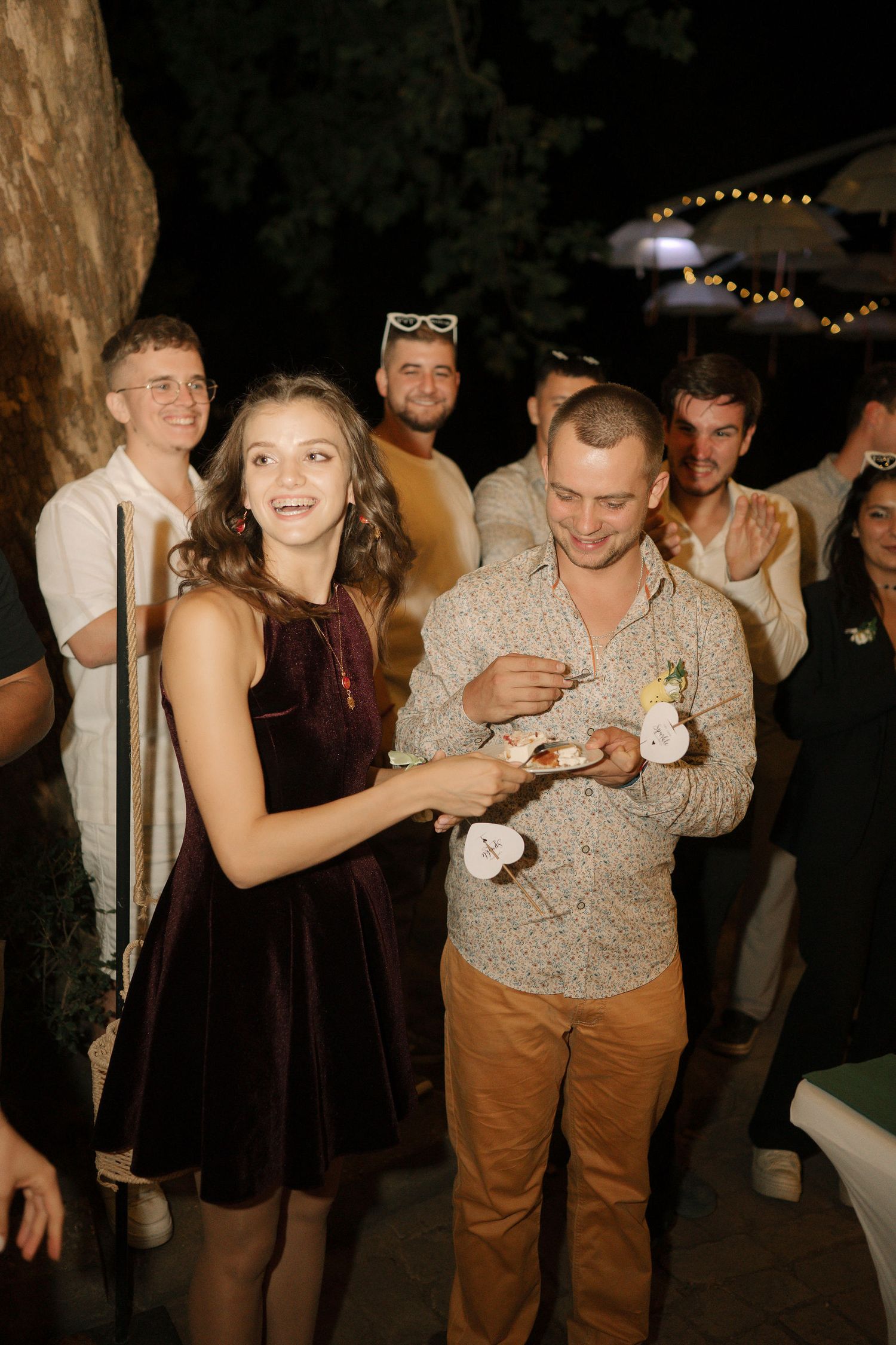 People dance and socialize at a nighttime party with string lights visible in the background.
