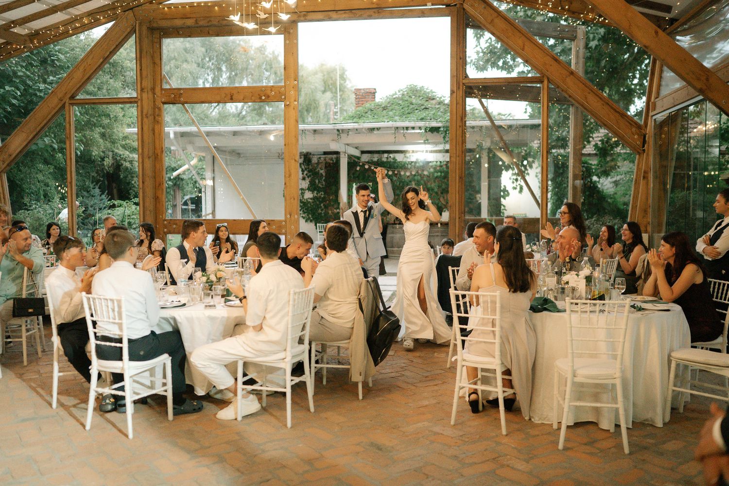 Wedding reception guests dance and celebrate under a rustic wooden pavilion decorated with string lights.