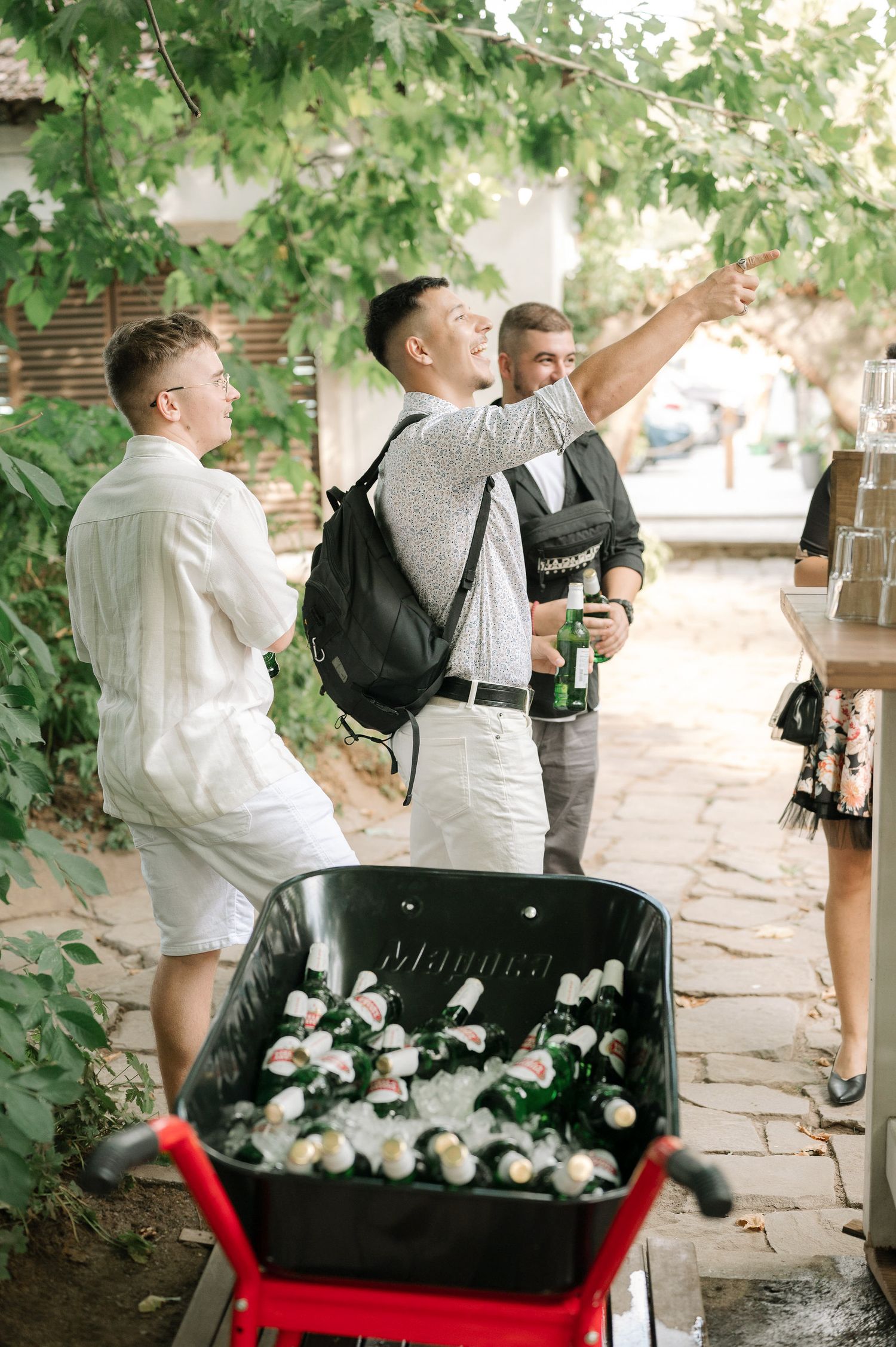 Wedding guests gather around a black piano decorated with white flowers in an outdoor garden setting.