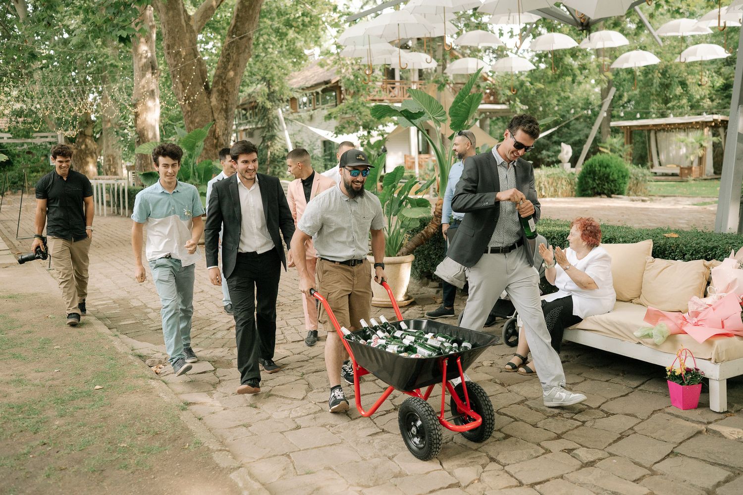 Group of friends walking together at an outdoor garden party with a wheelbarrow full of drinks and refreshments.