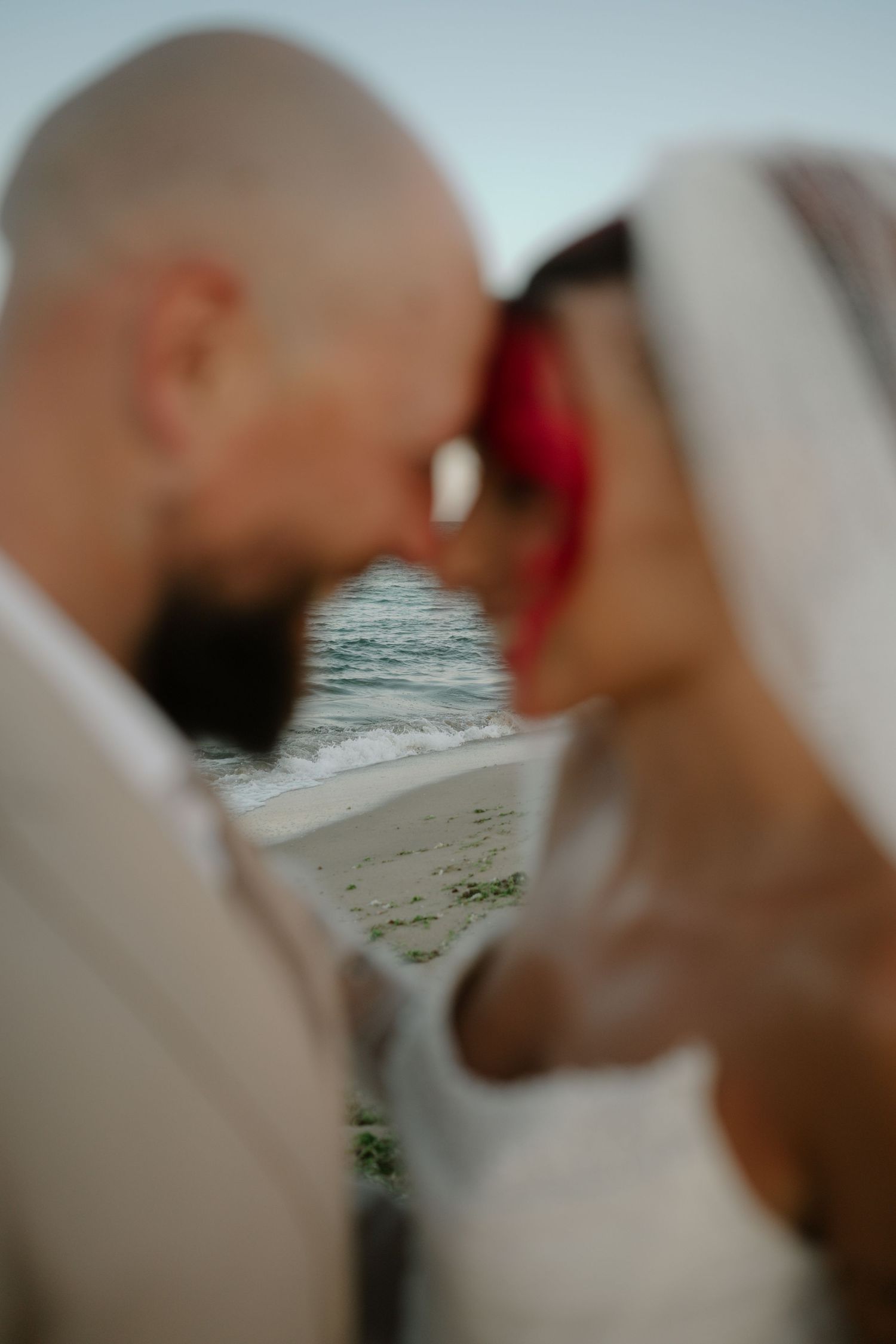 A romantic couple shares a tender moment on the beach at sunset with ocean waves in the background.