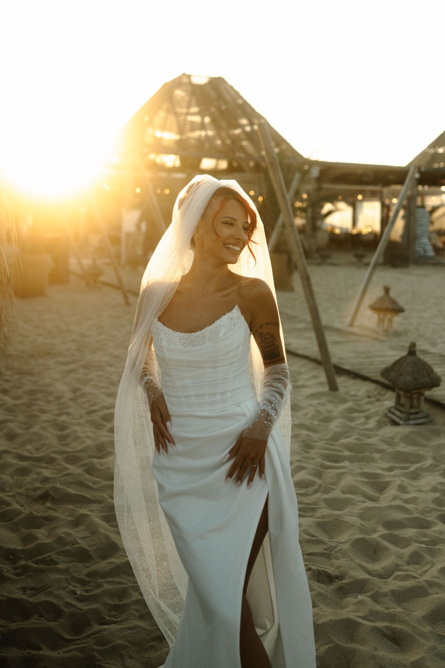 A person in a flowing white dress poses gracefully on a sandy beach at sunset.