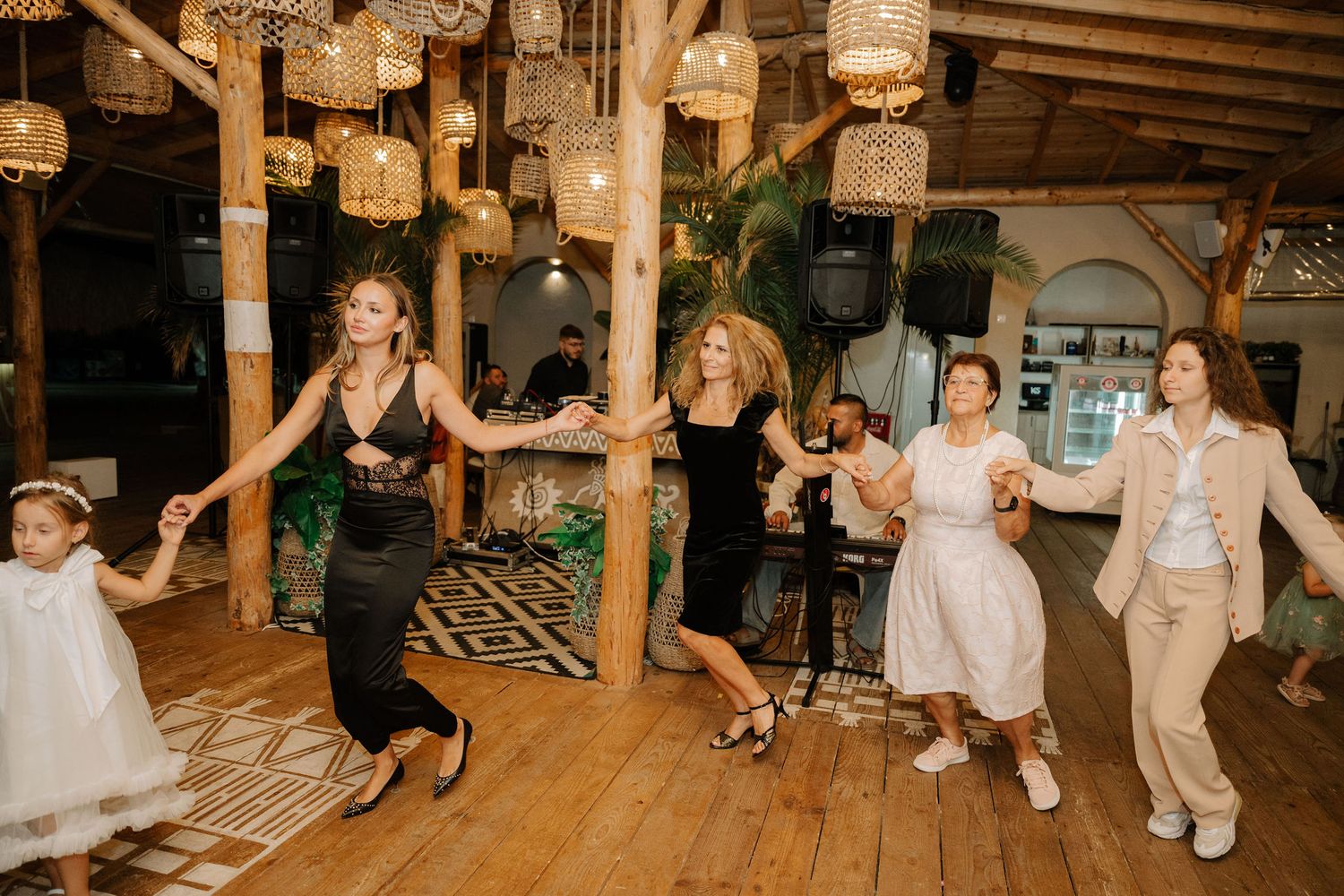 Wedding guests dance and celebrate on a rustic wooden dance floor under hanging lantern lights at an evening reception.