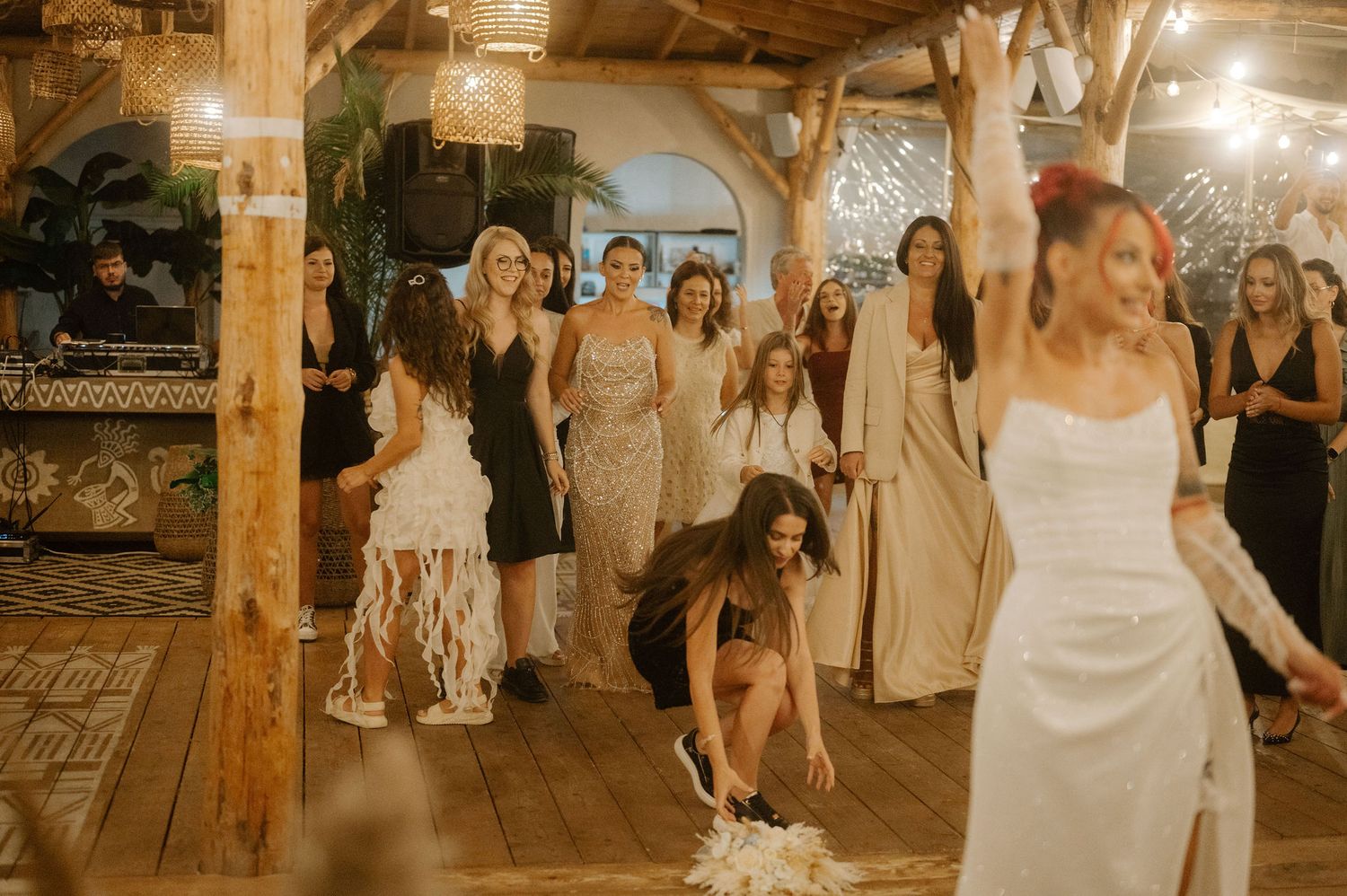 Wedding guests dance and celebrate on a rustic wooden dance floor in a warmly lit barn venue.