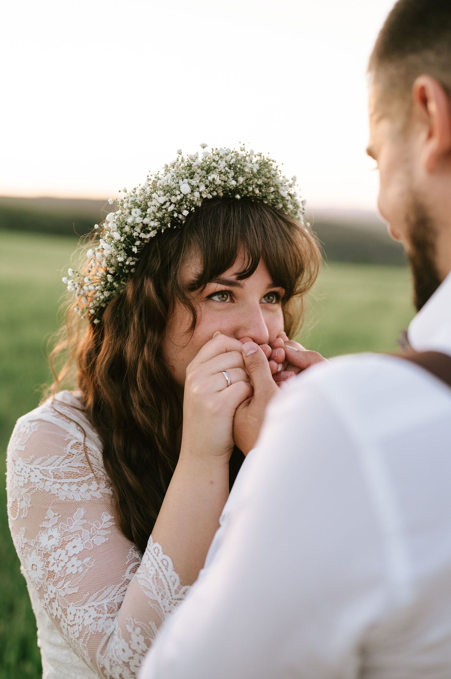 A bride wearing a lace dress and flower crown shows emotion during an outdoor photo session.