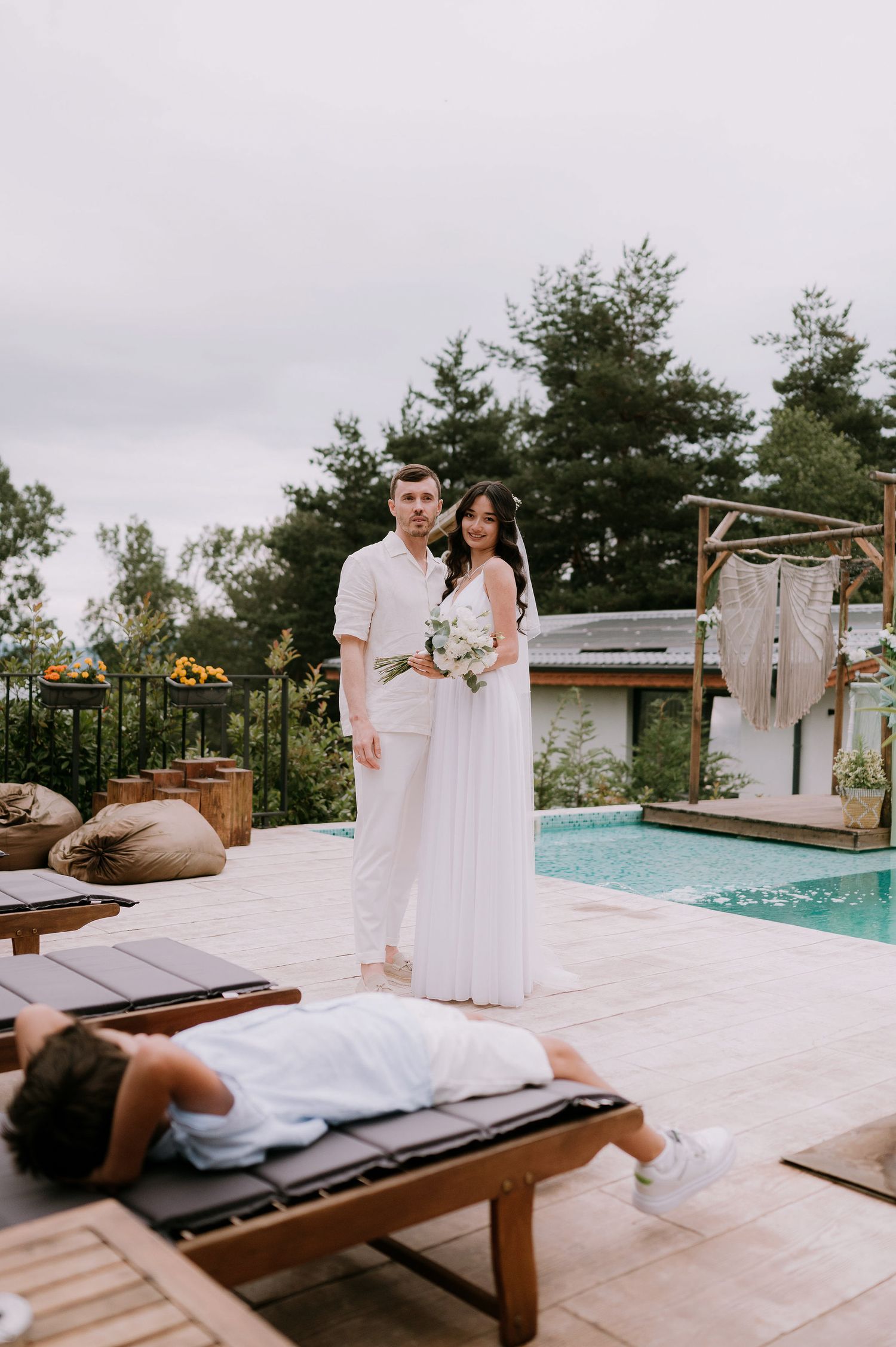 A romantic poolside wedding photoshoot with couple in all white attire sharing intimate moments on a wooden deck.