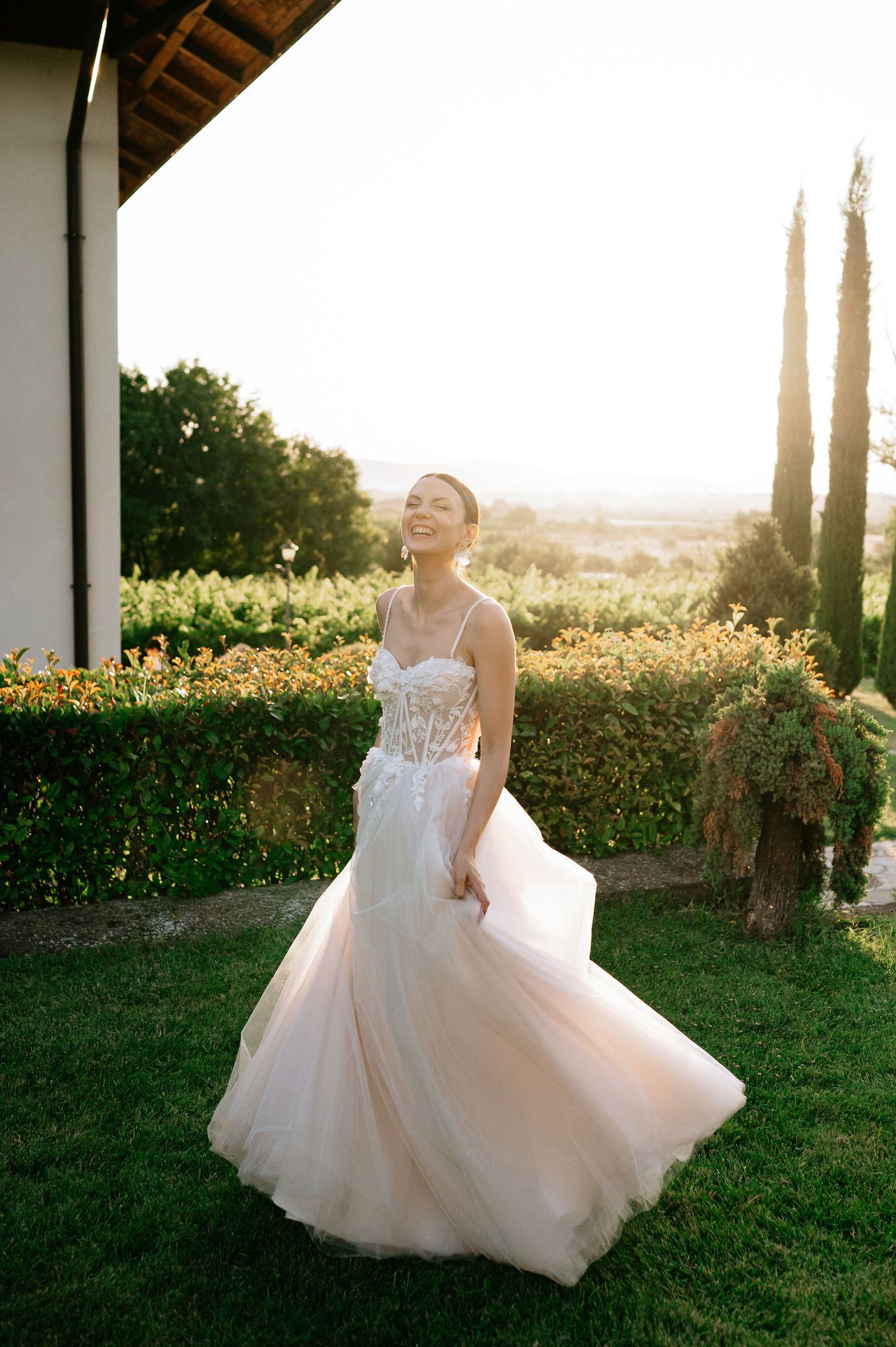 Bride in flowing tulle gown twirls joyfully in a garden during golden hour.