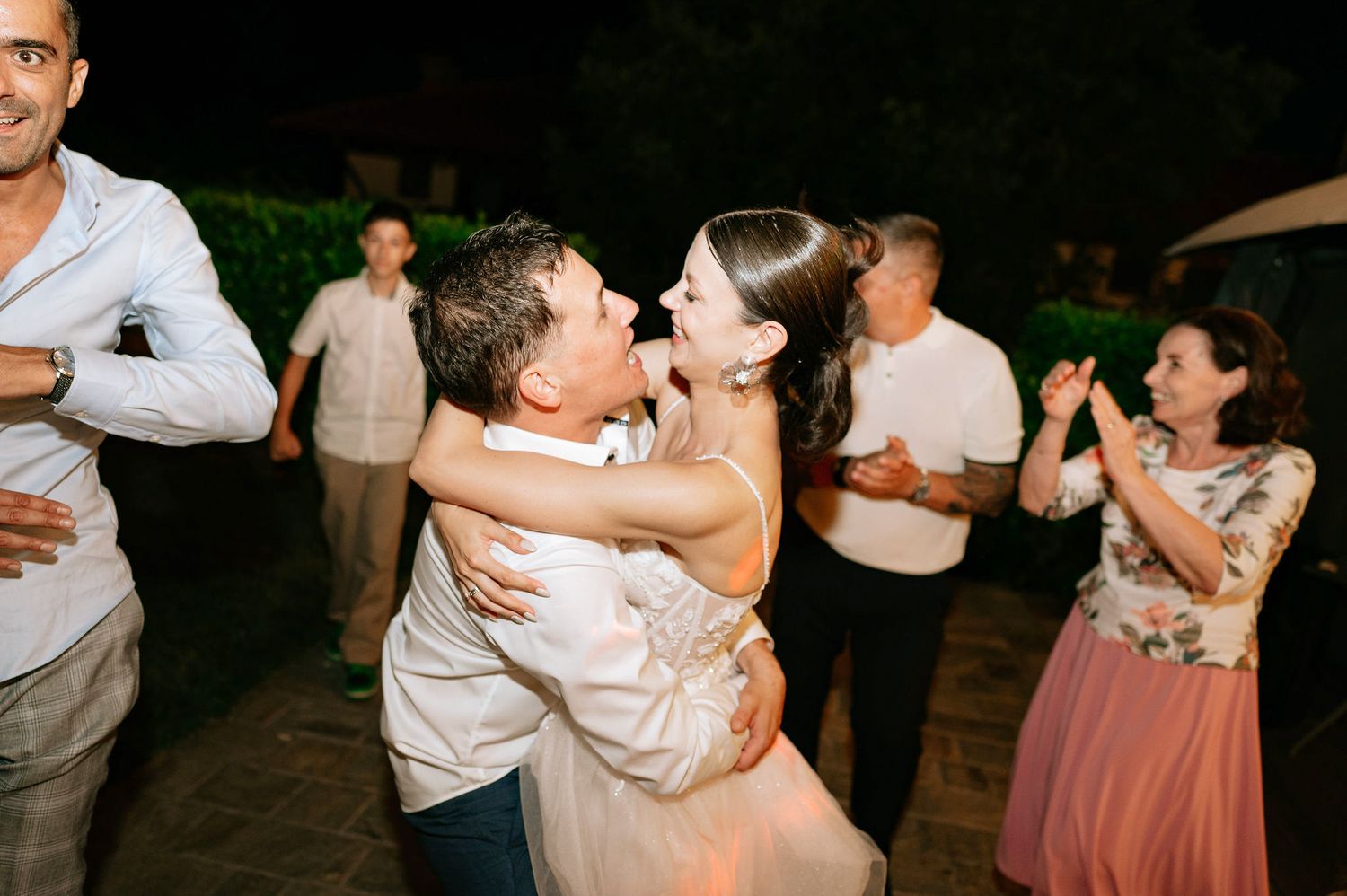Couples dancing together at an outdoor evening celebration with string lights overhead.