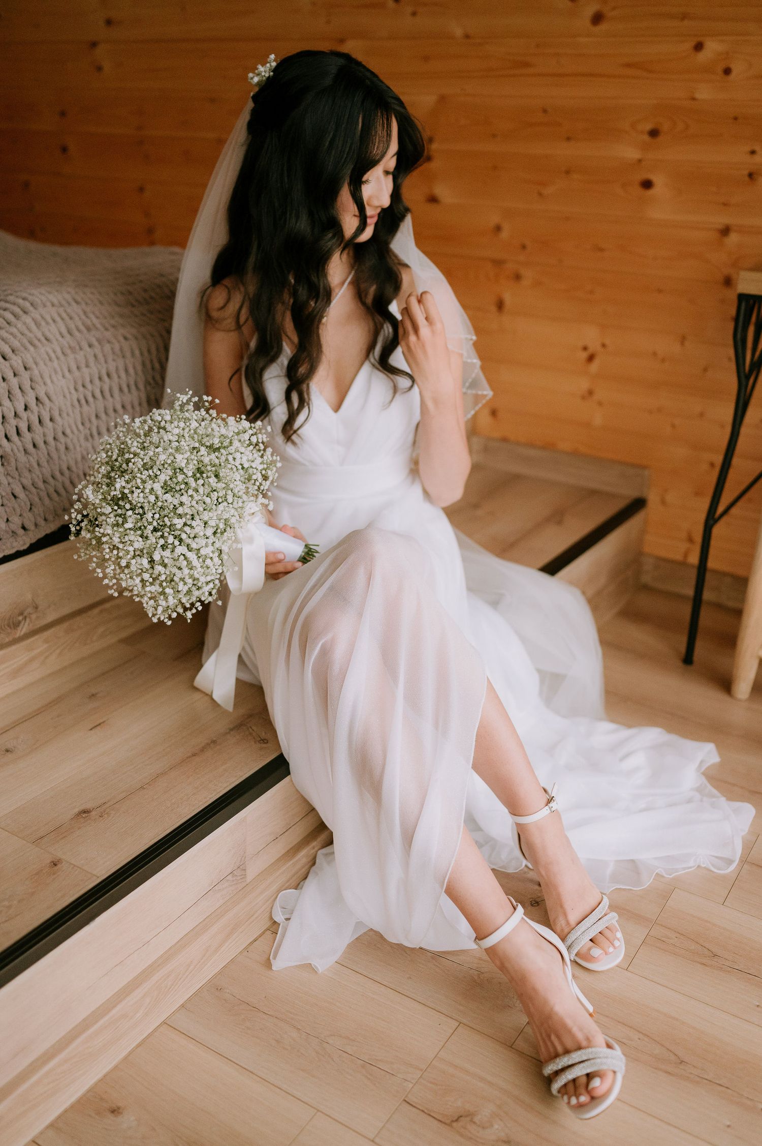 Artistic bridal portrait on wooden floor with flowing white gown and baby's breath bouquet.