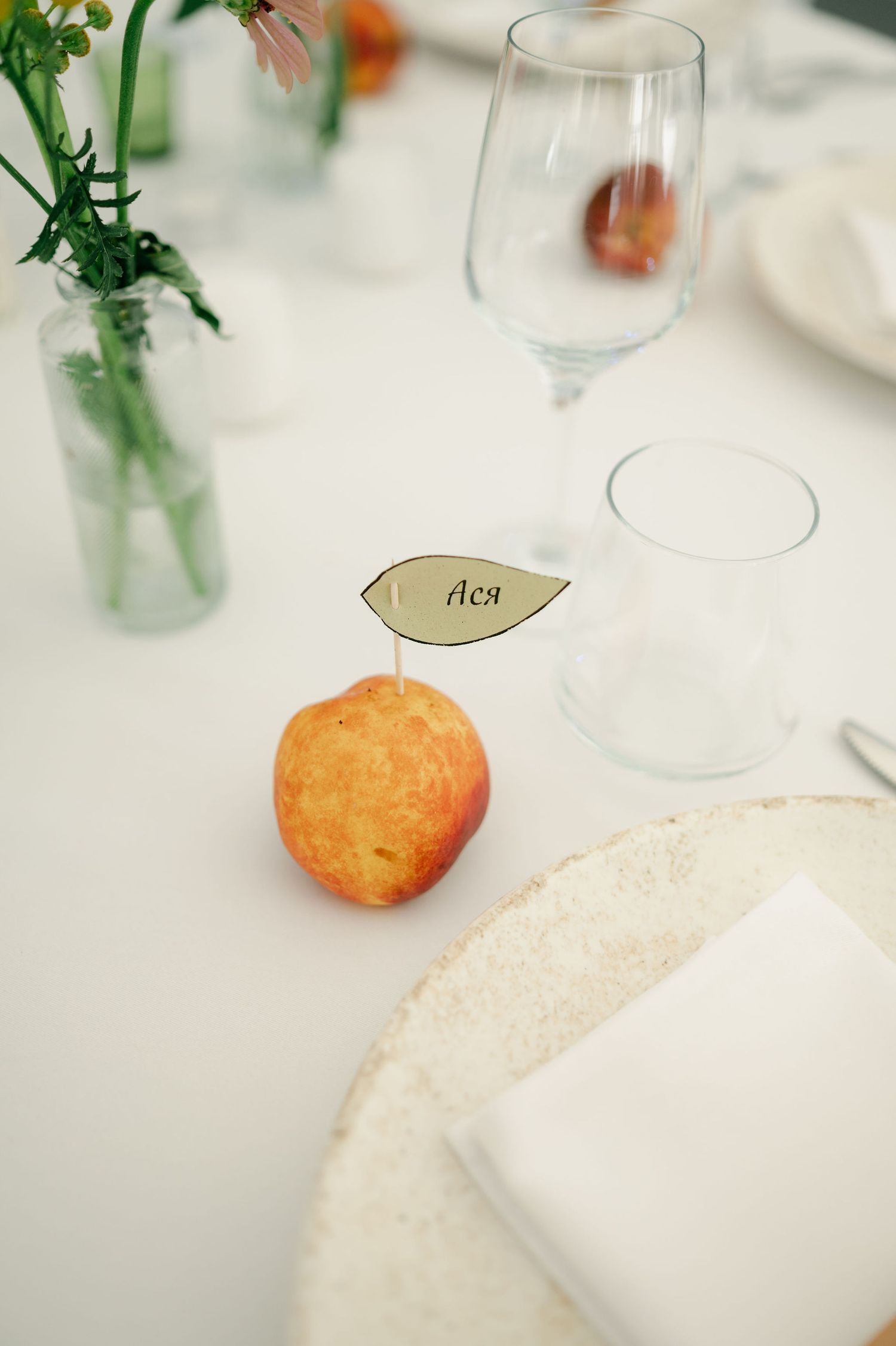 Wedding table details showing place settings with orange fruit accents and delicate floral arrangements.