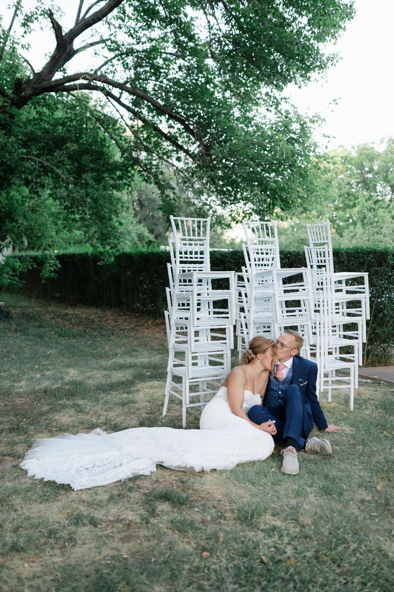 Wedding couple embraces on grassy ground with elegant white ceremony chairs behind them.