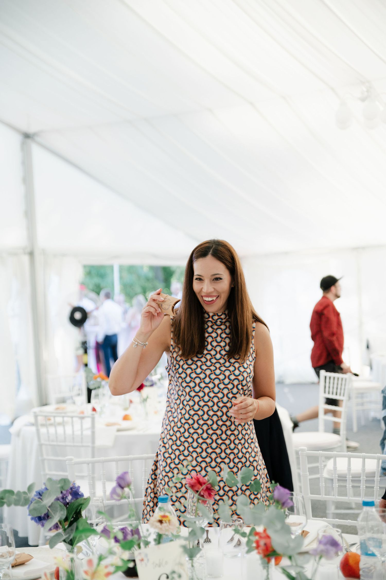 Wedding reception setup in white tent with colorful floral arrangements and table decorations.