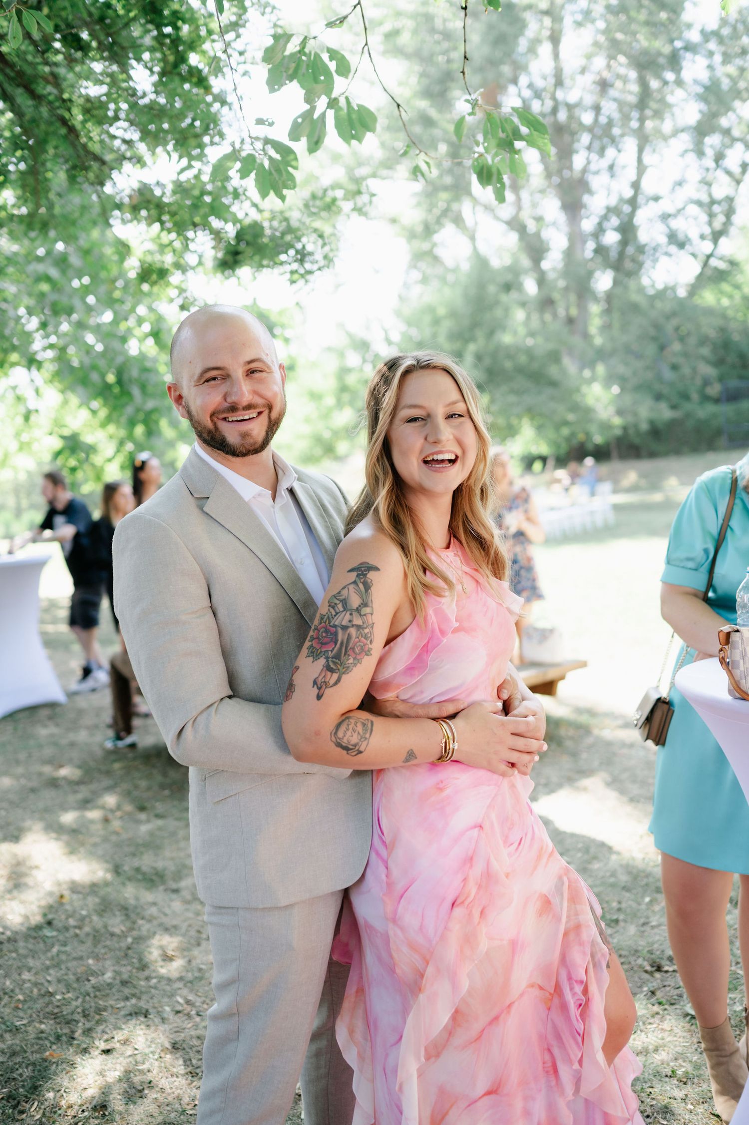 Couple sharing joyful moments at an outdoor celebration wearing pink and grey formal attire.
