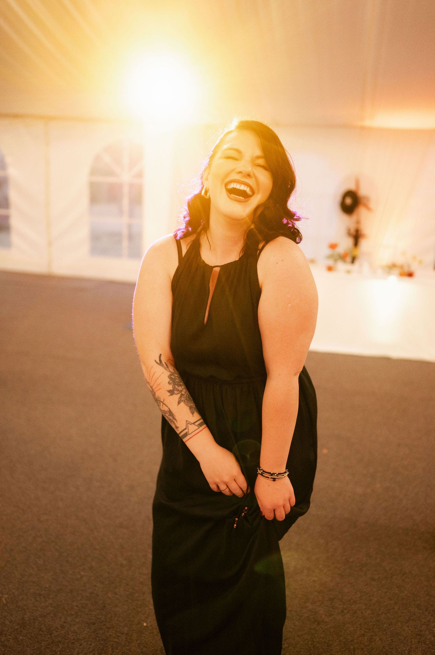 Person in black dress laughs joyfully during wedding reception celebration.