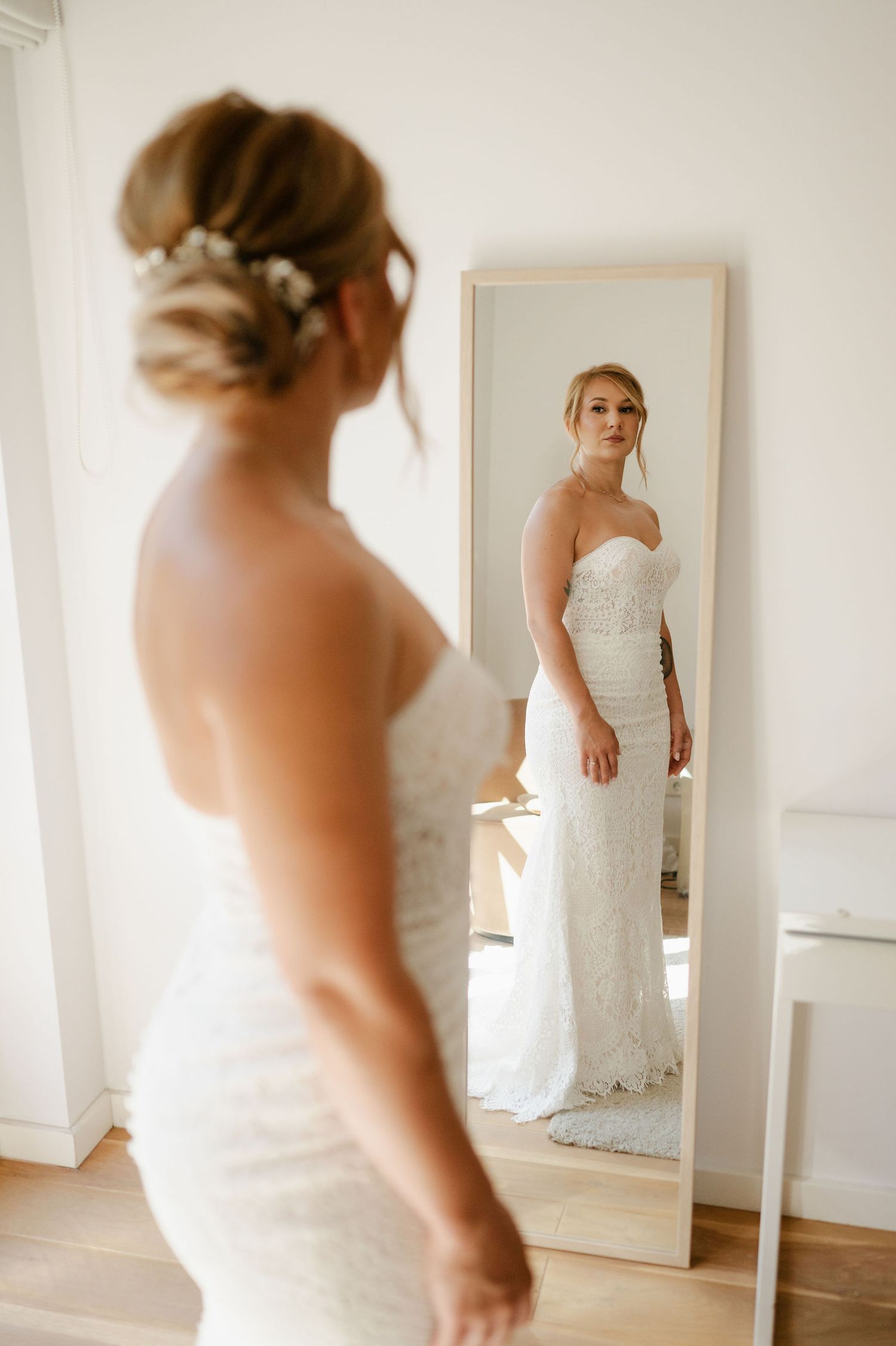 Full-length mirror reflection of bride in fitted lace wedding dress.