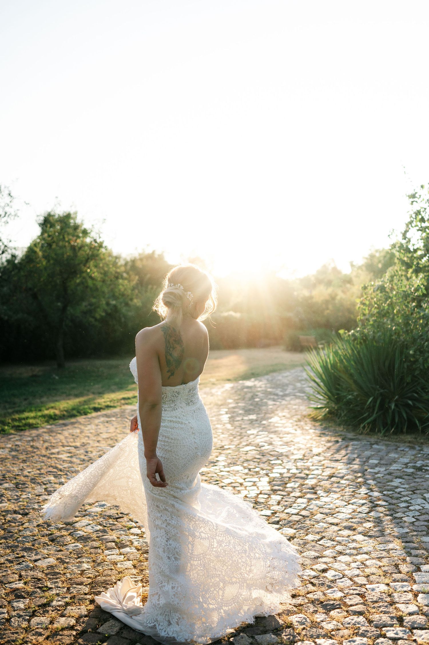 Beautiful lace wedding gown photographed on stone path during golden hour.