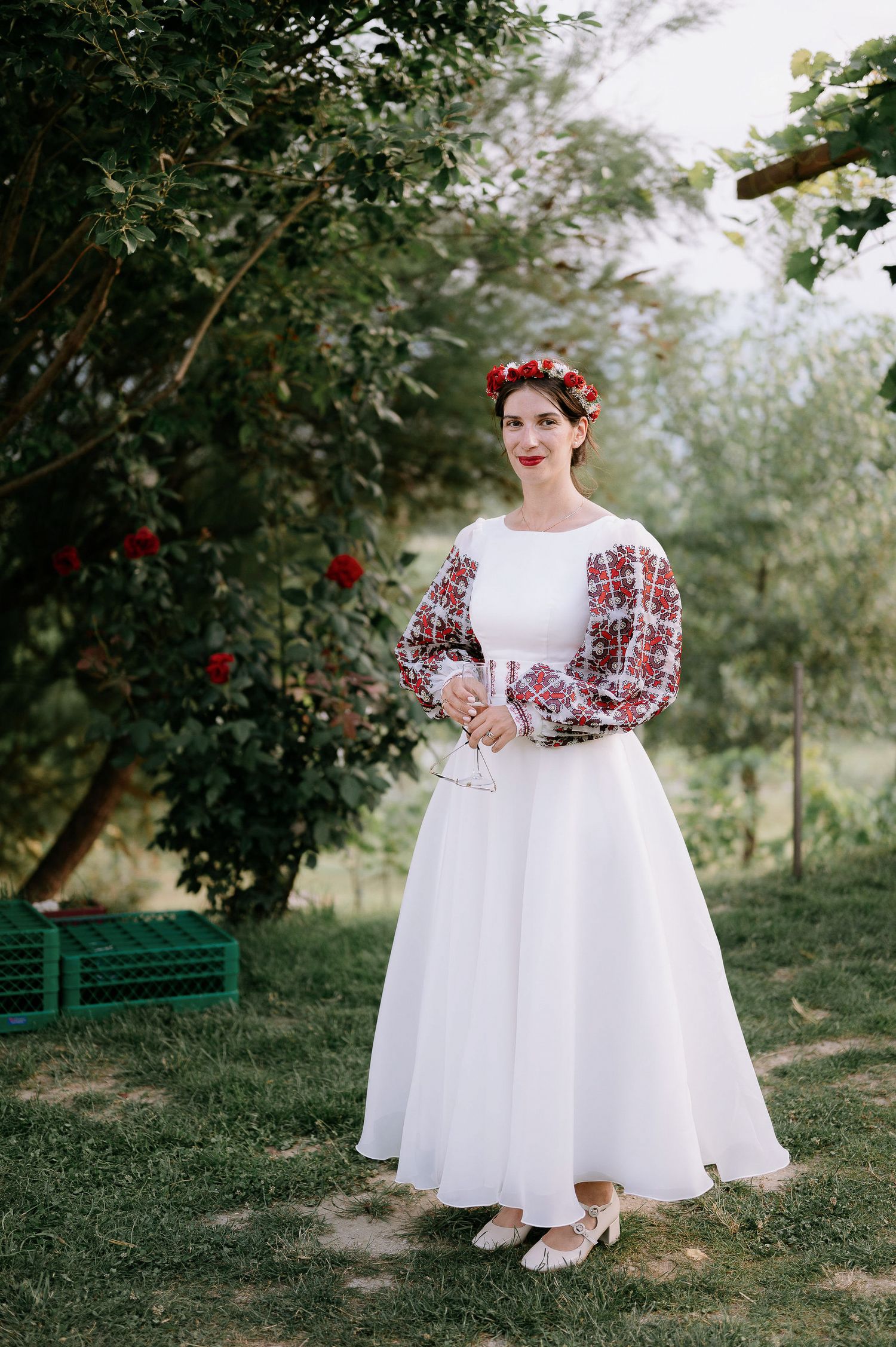 A white wedding gown with traditional red embroidered sleeves captured in a natural outdoor setting.