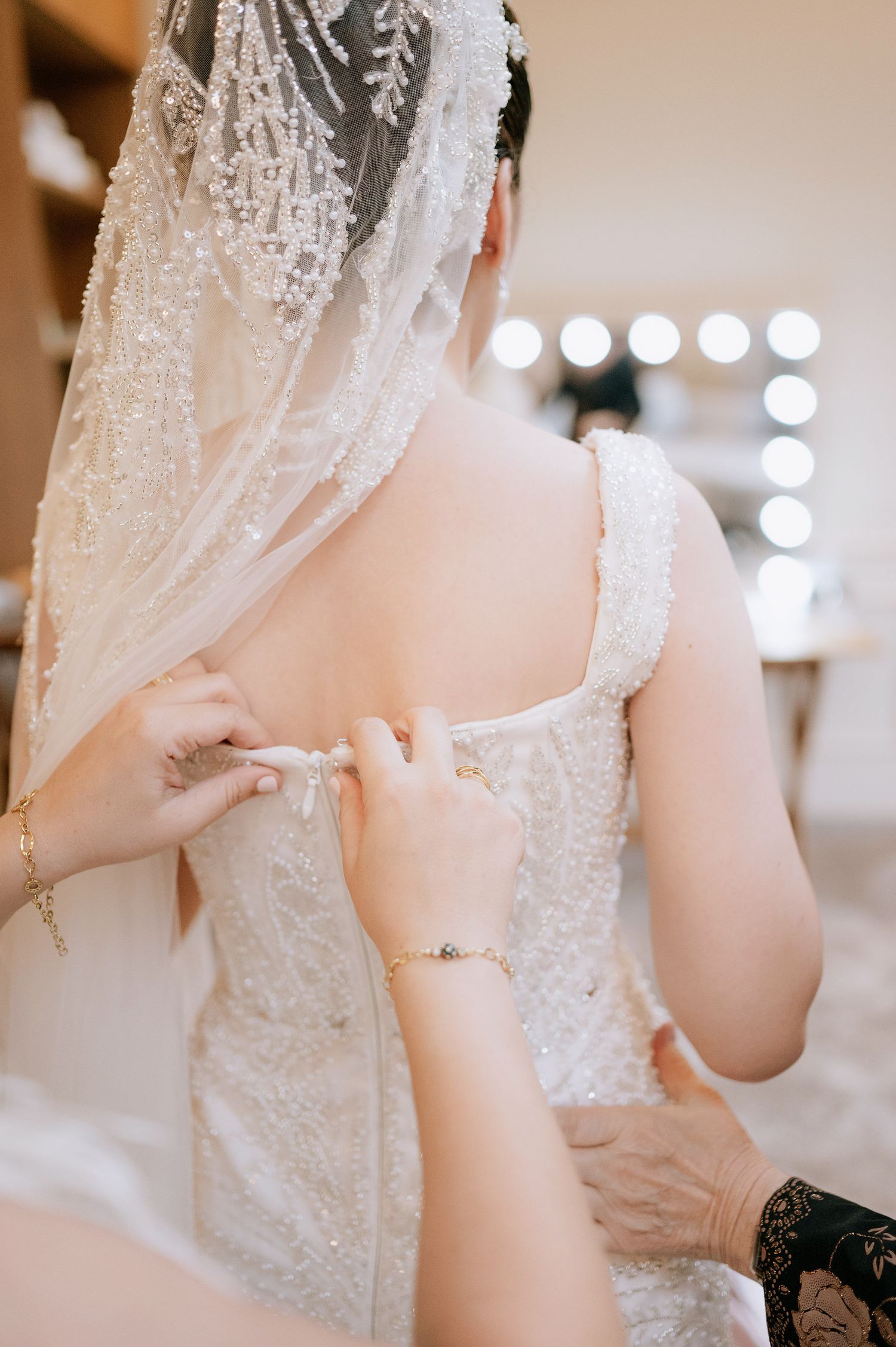 Close-up of hands fastening delicate lace buttons on back of wedding dress.
