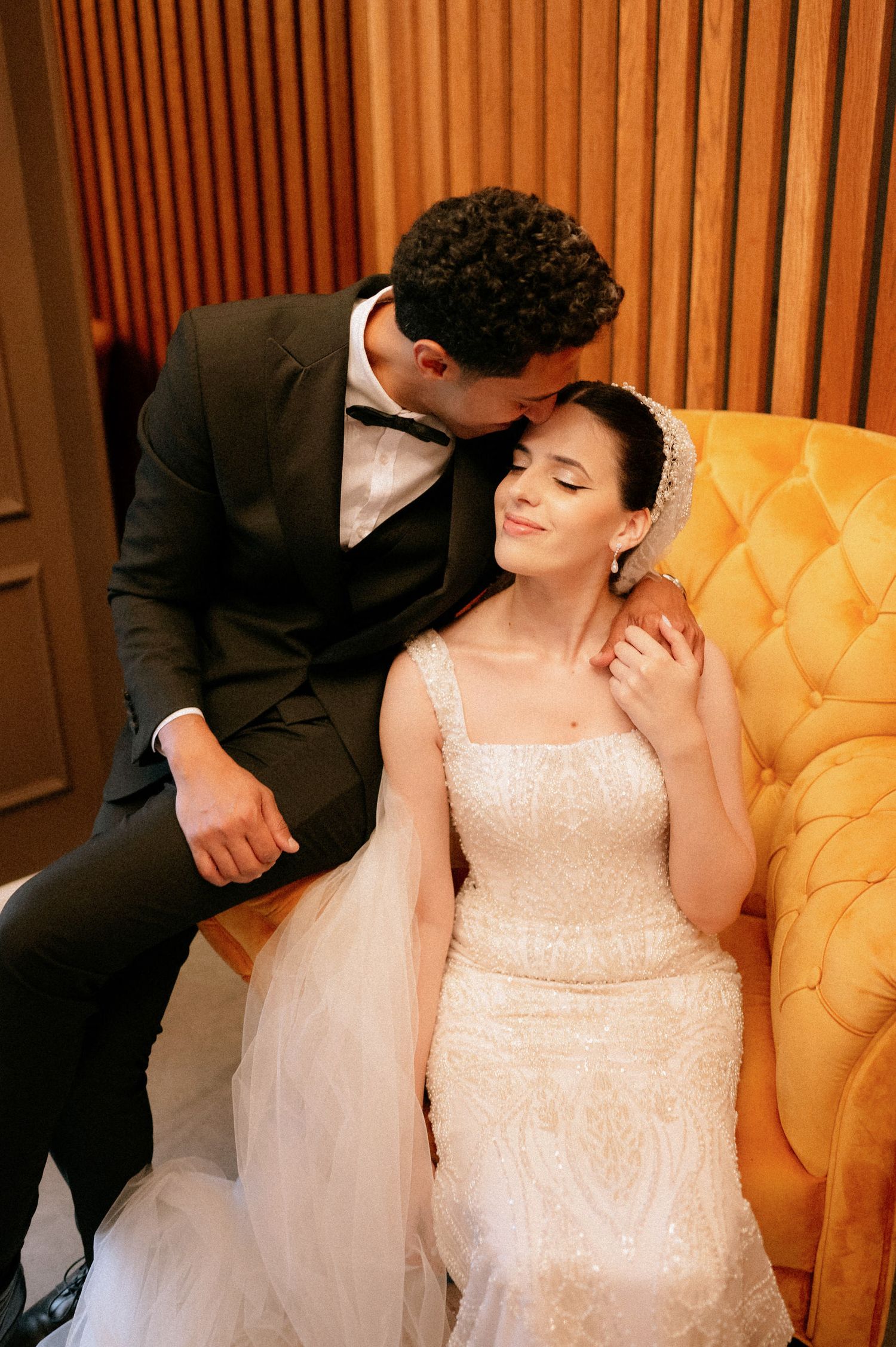 Romantic moment on a yellow tufted couch with wood paneled walls in the background.