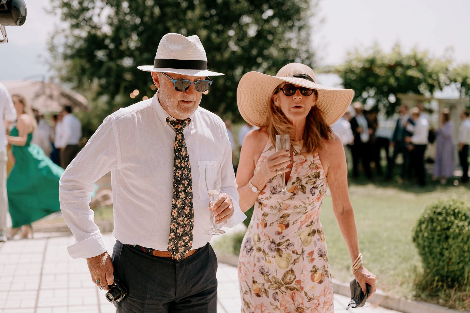 Wedding guests mingle outdoors at a garden reception on a sunny afternoon.