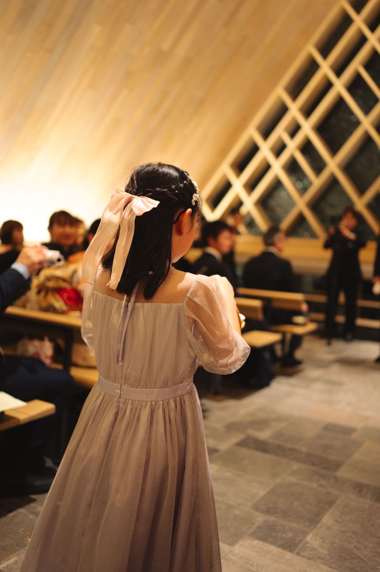 Flower girl in empire waist dress walking through modern chapel venue.