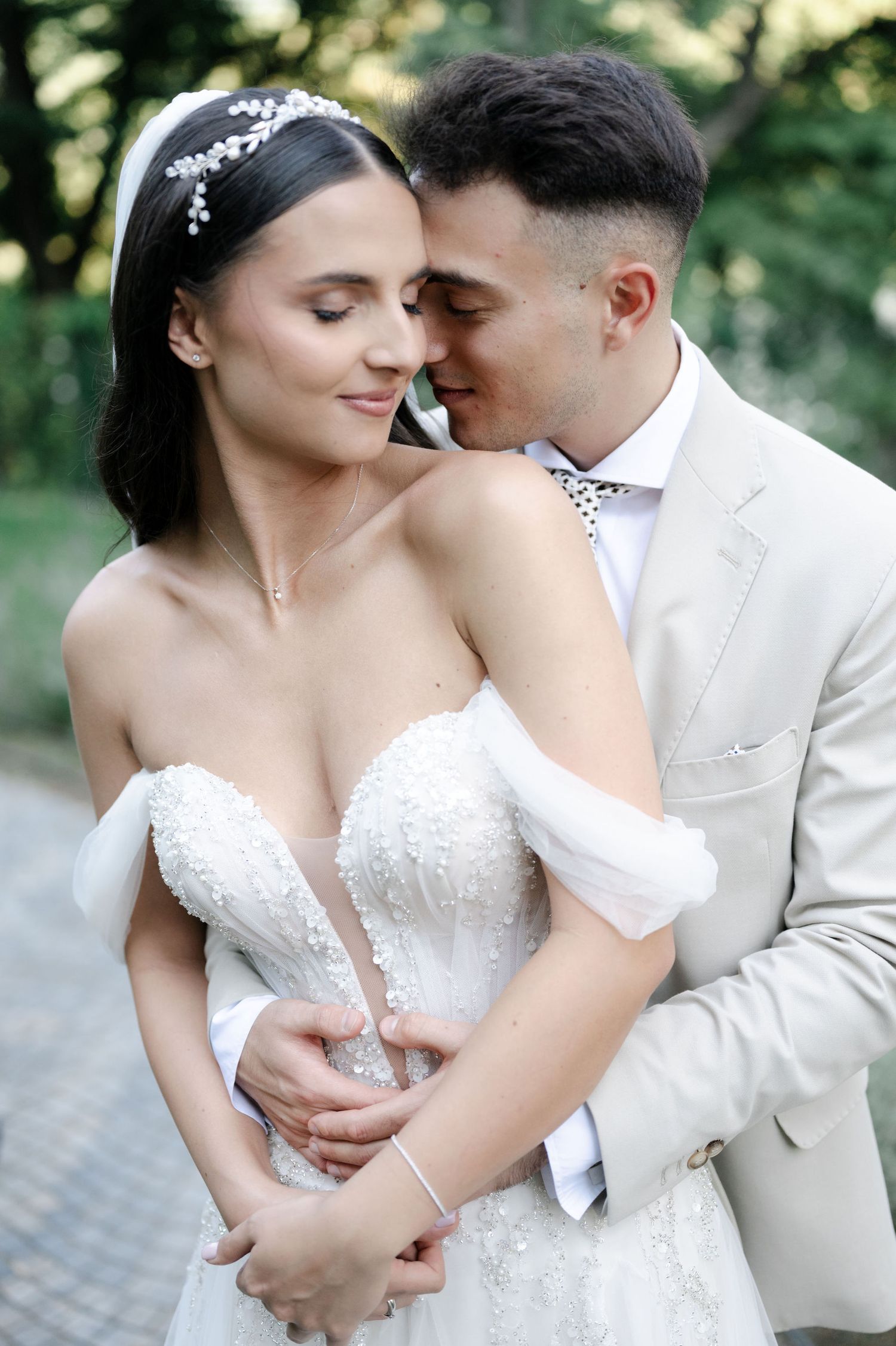 Romantic wedding couple embraces in an intimate moment outdoors with natural greenery backdrop.