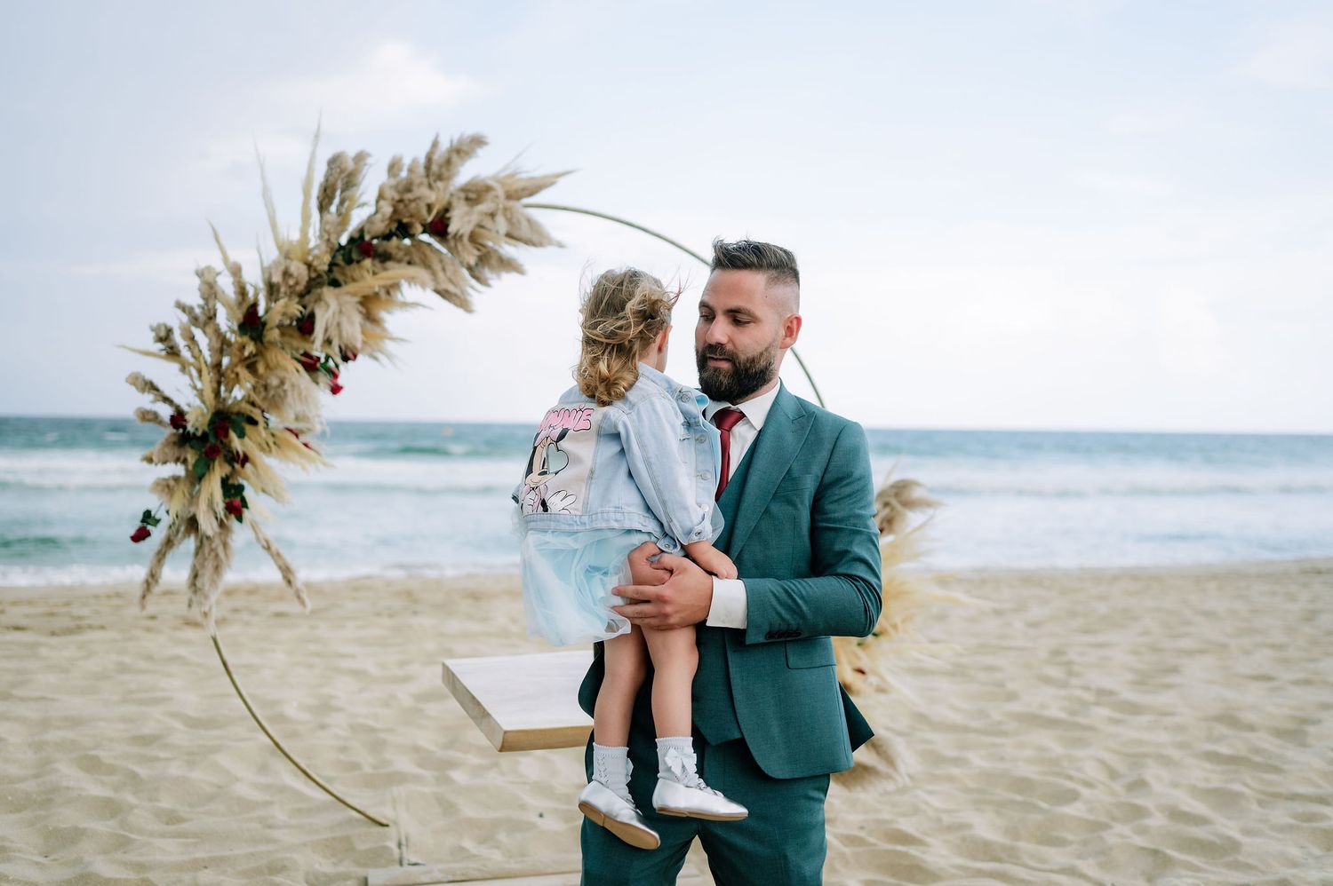 Couple holding dried palm fronds on sandy beach during wedding ceremony.