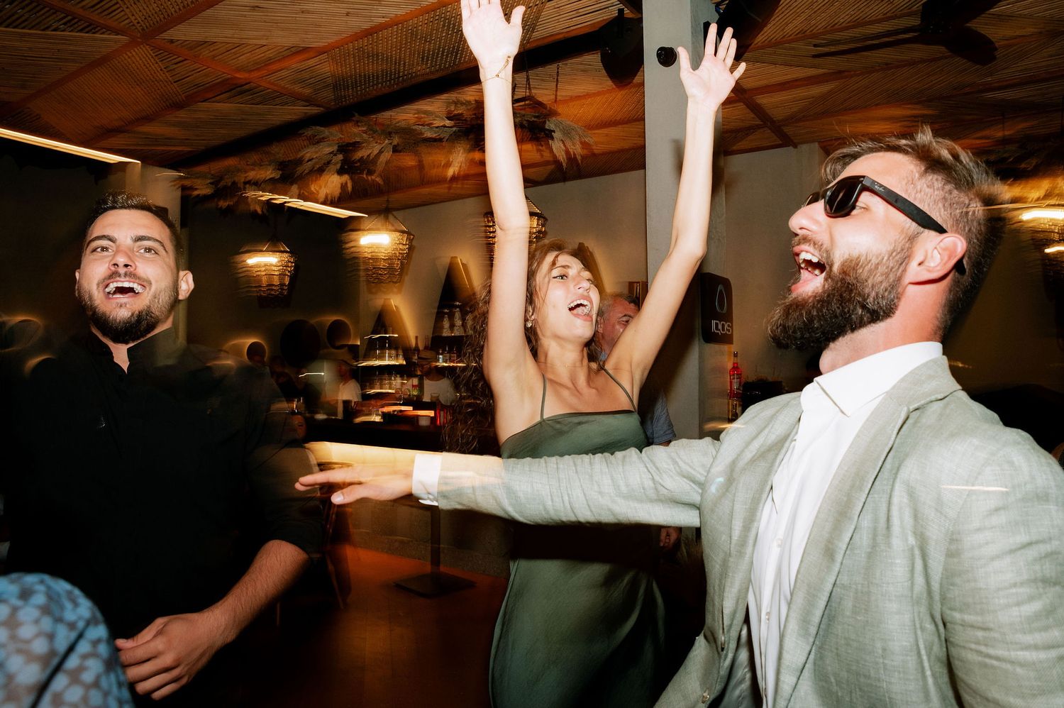 Enthusiastic partygoers with raised arms dancing and celebrating under warm lighting.