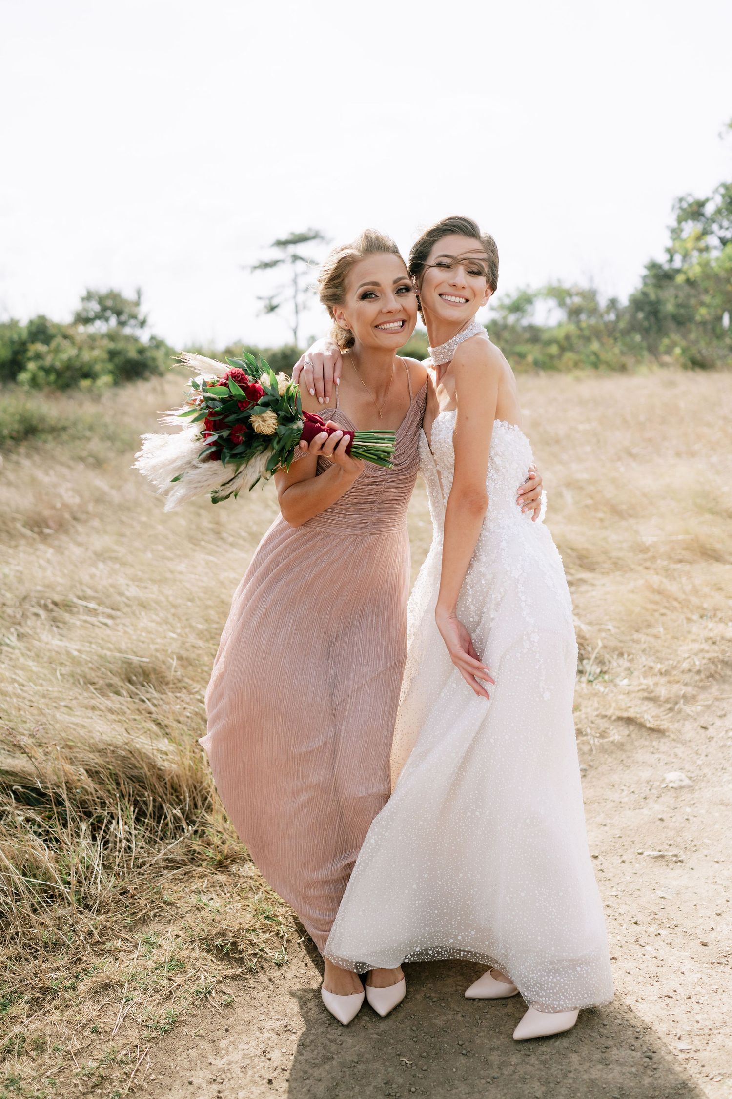 Two people in formal wear embrace while standing on a natural path.