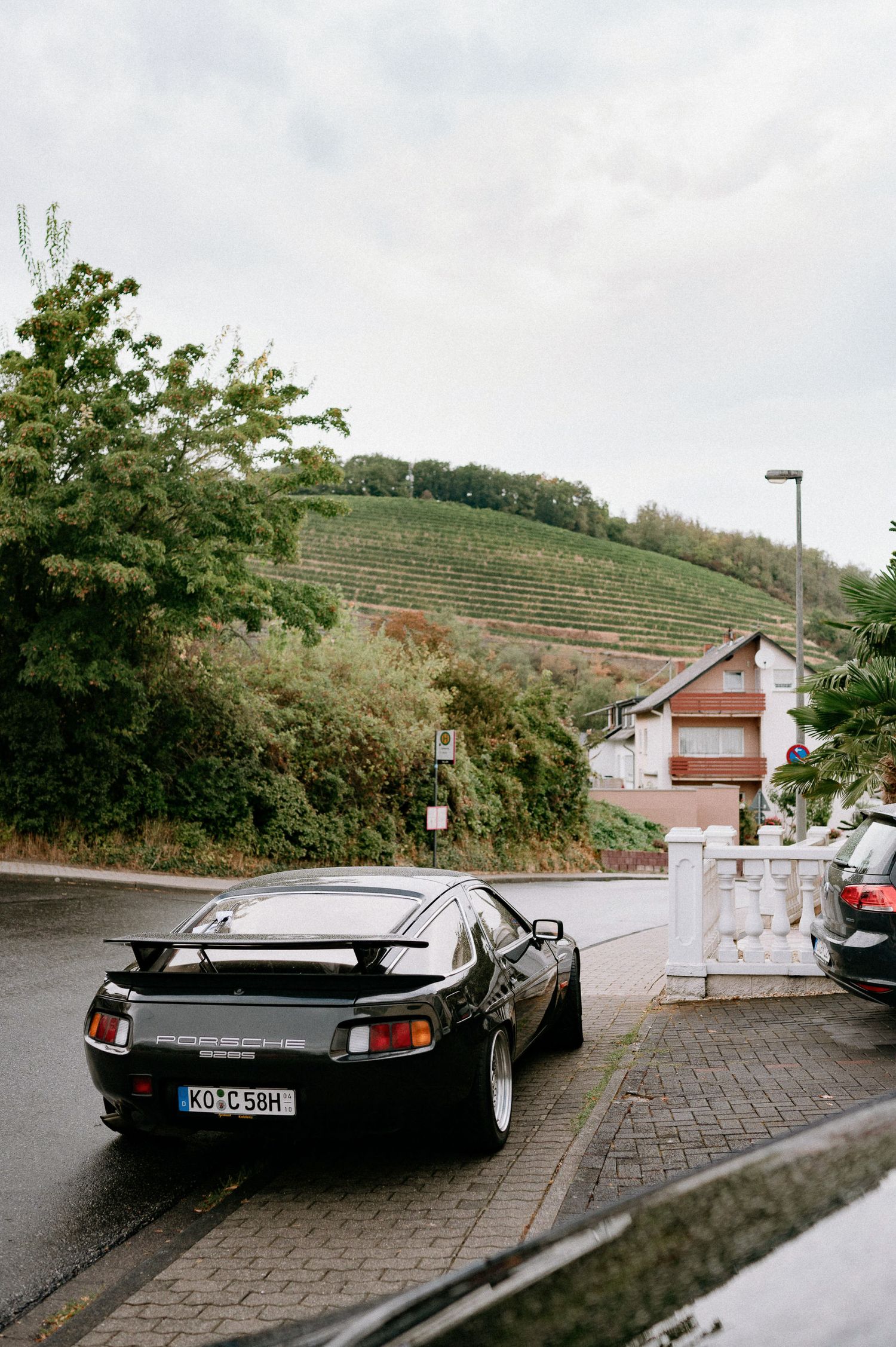 Modern black sports car parked on a hillside street with vineyards in the background.
