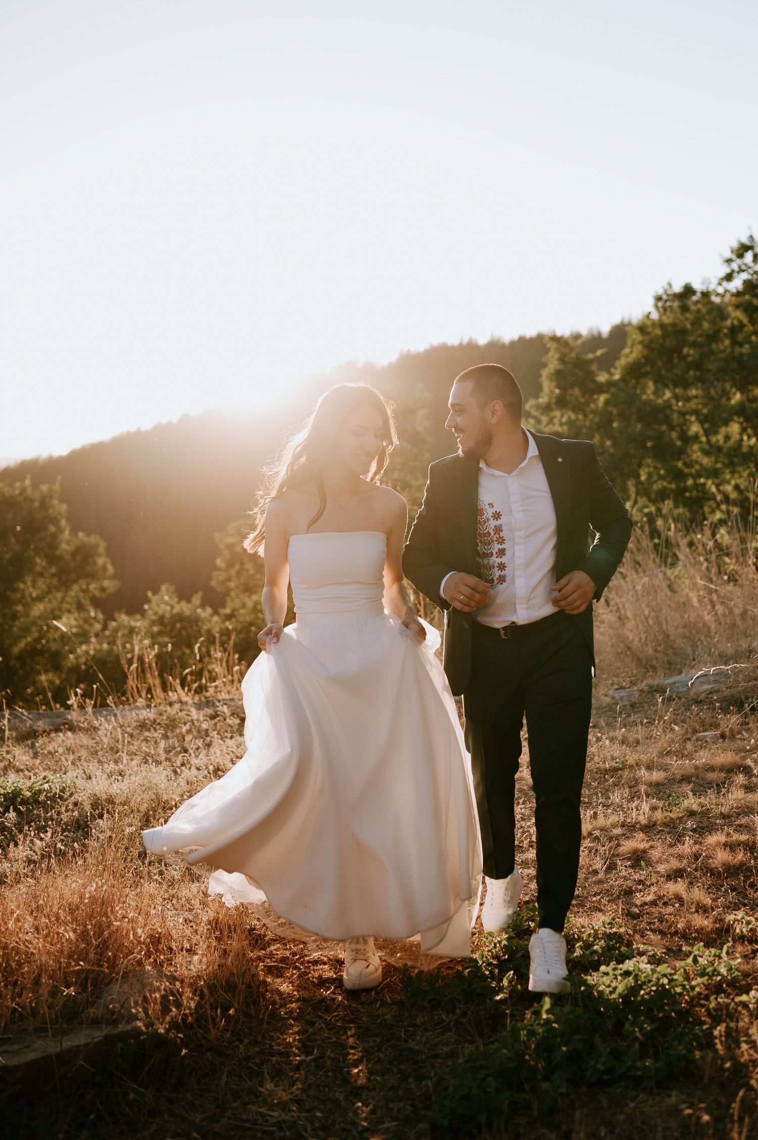 Candid moment of newlyweds walking together on sunlit mountainside path.