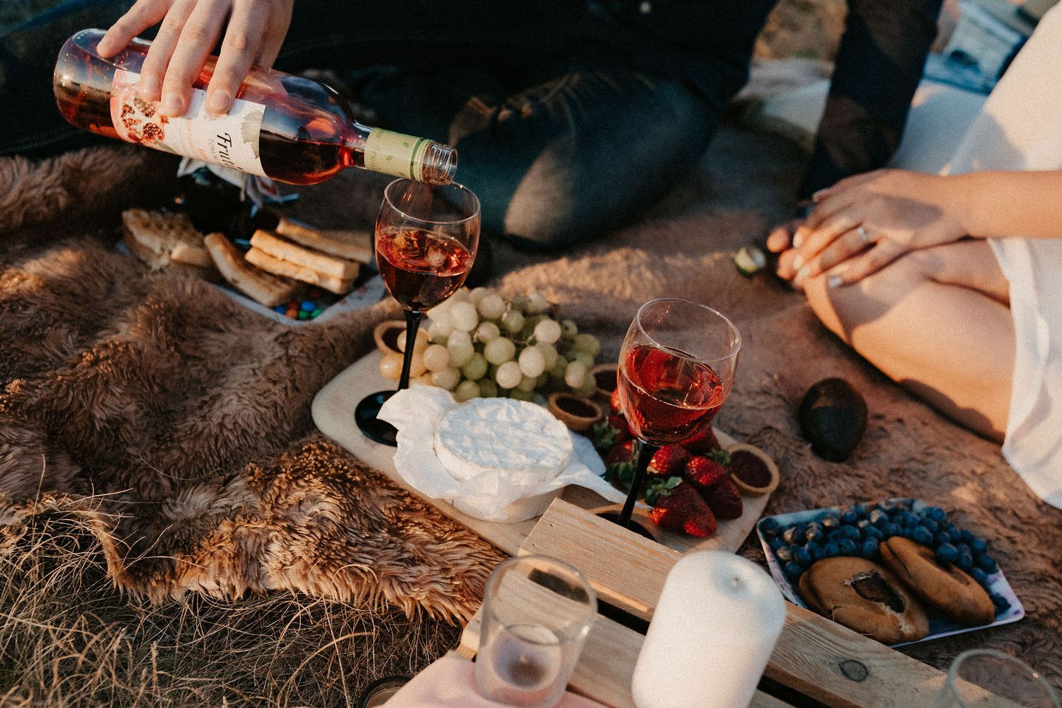 A romantic picnic spread with wine glasses, fresh fruits, and snacks laid out on a cozy blanket.