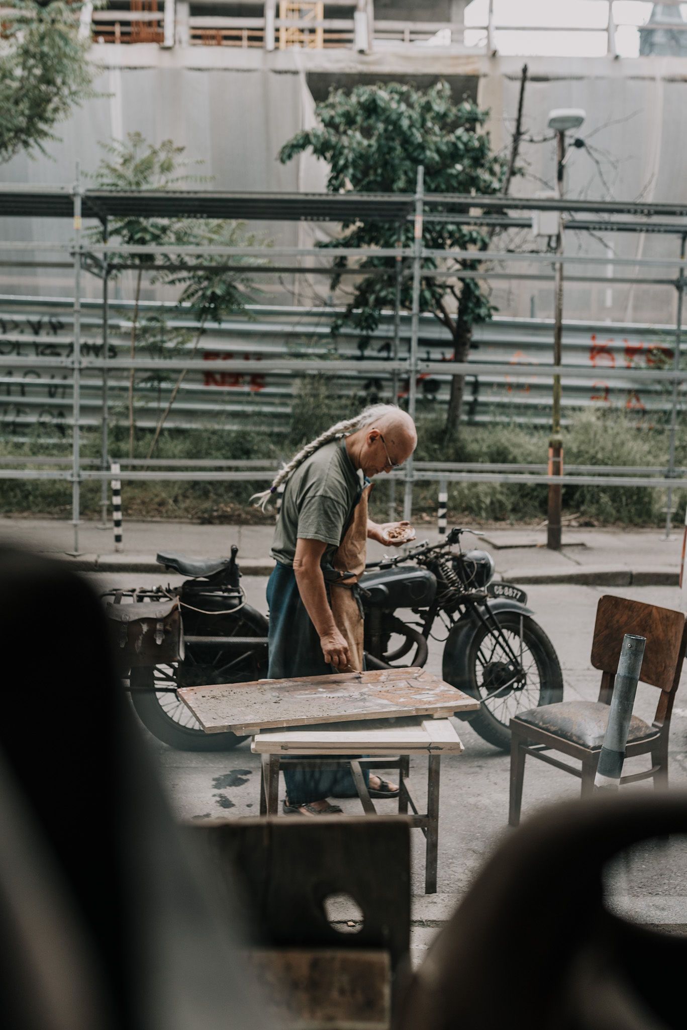 Person working on a project outdoors with benches and buildings in the background.