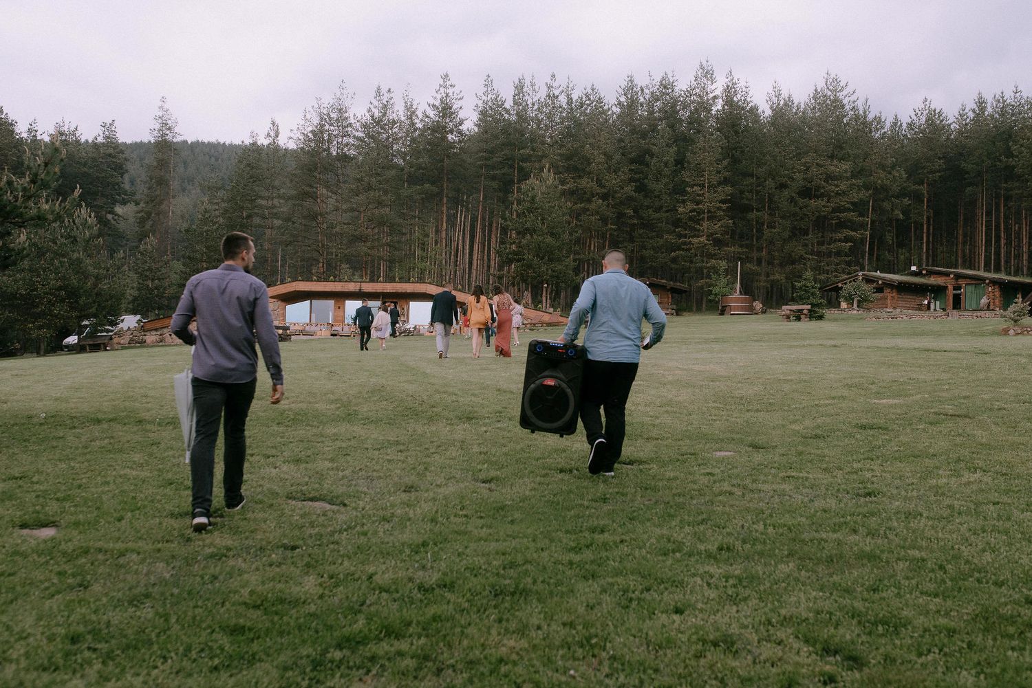 Group walking through an open field with pine forest backdrop on overcast day.