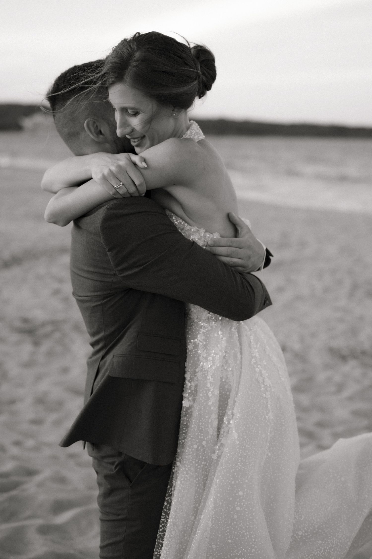 Black and white photo of bride and groom embracing on sandy beach.