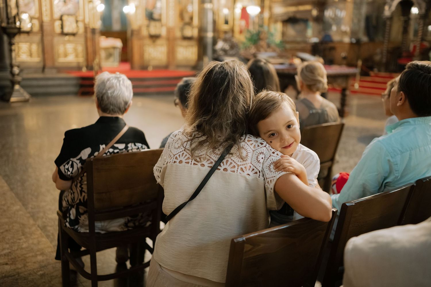 A group of people sitting in wooden pews during a church service, with warm lighting illuminating the interior space.